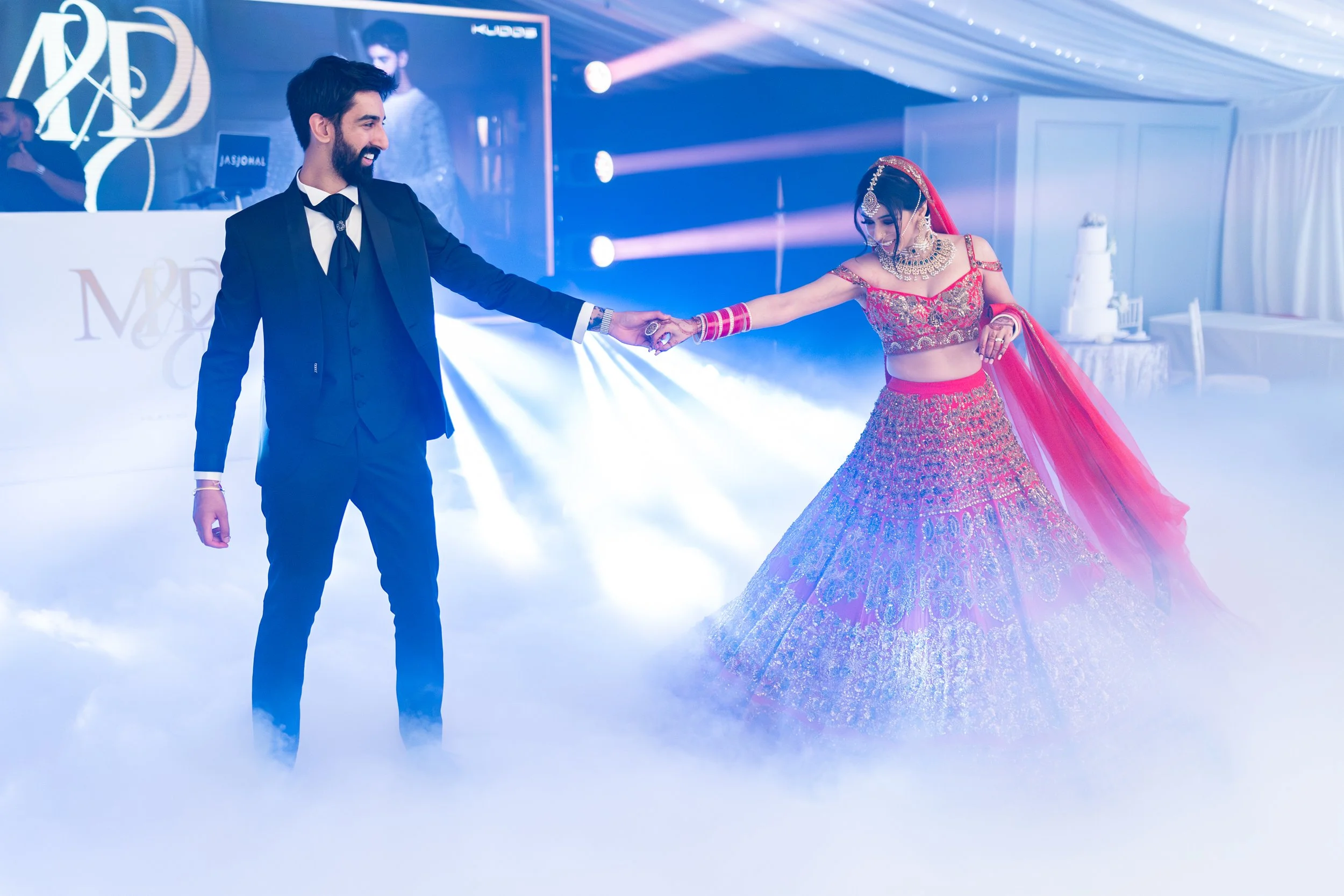 A bride and groom dancing at their wedding reception surrounded by fog and blue lighting.