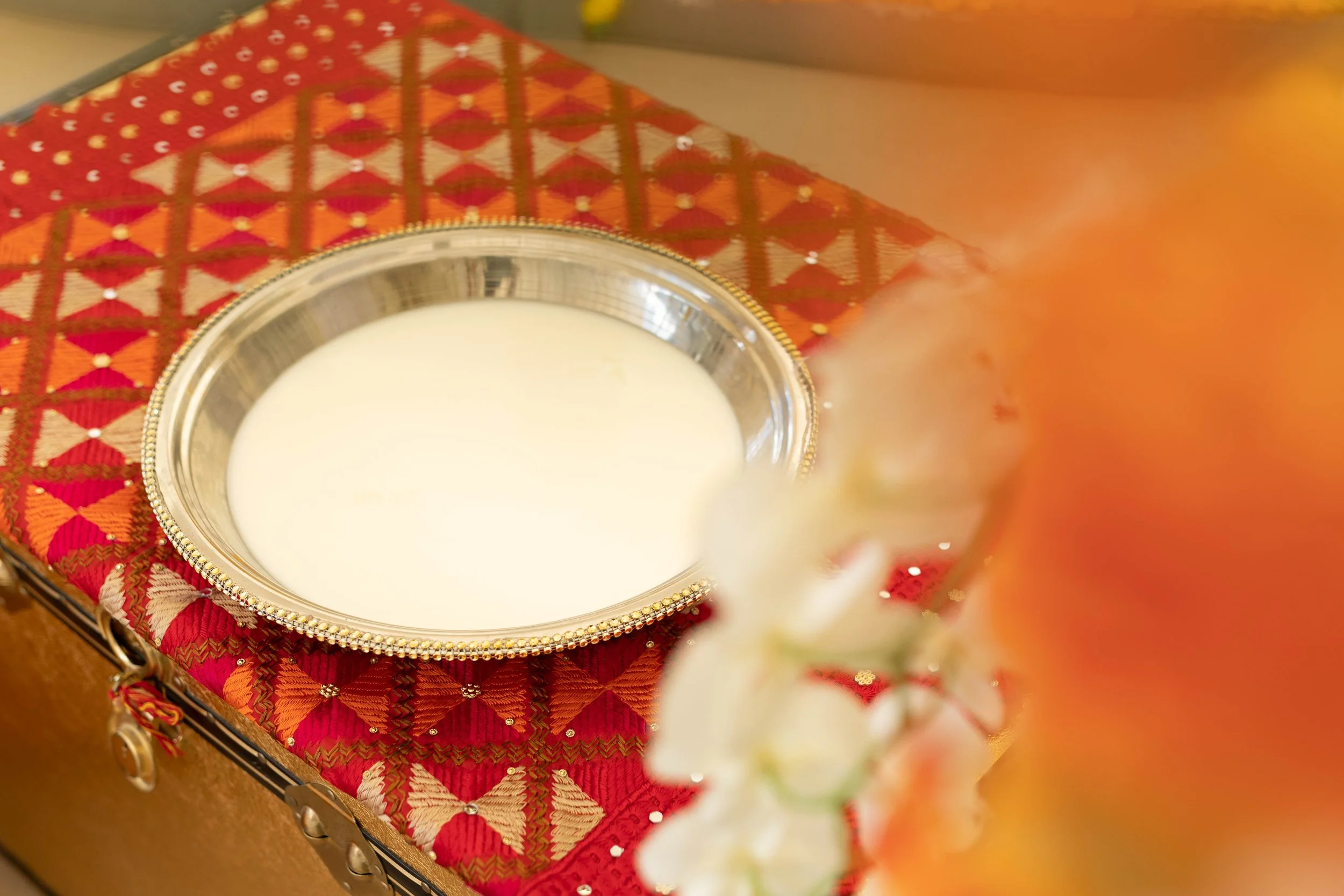 A silver bowl filled with white liquid, placed on a red and gold patterned cloth.