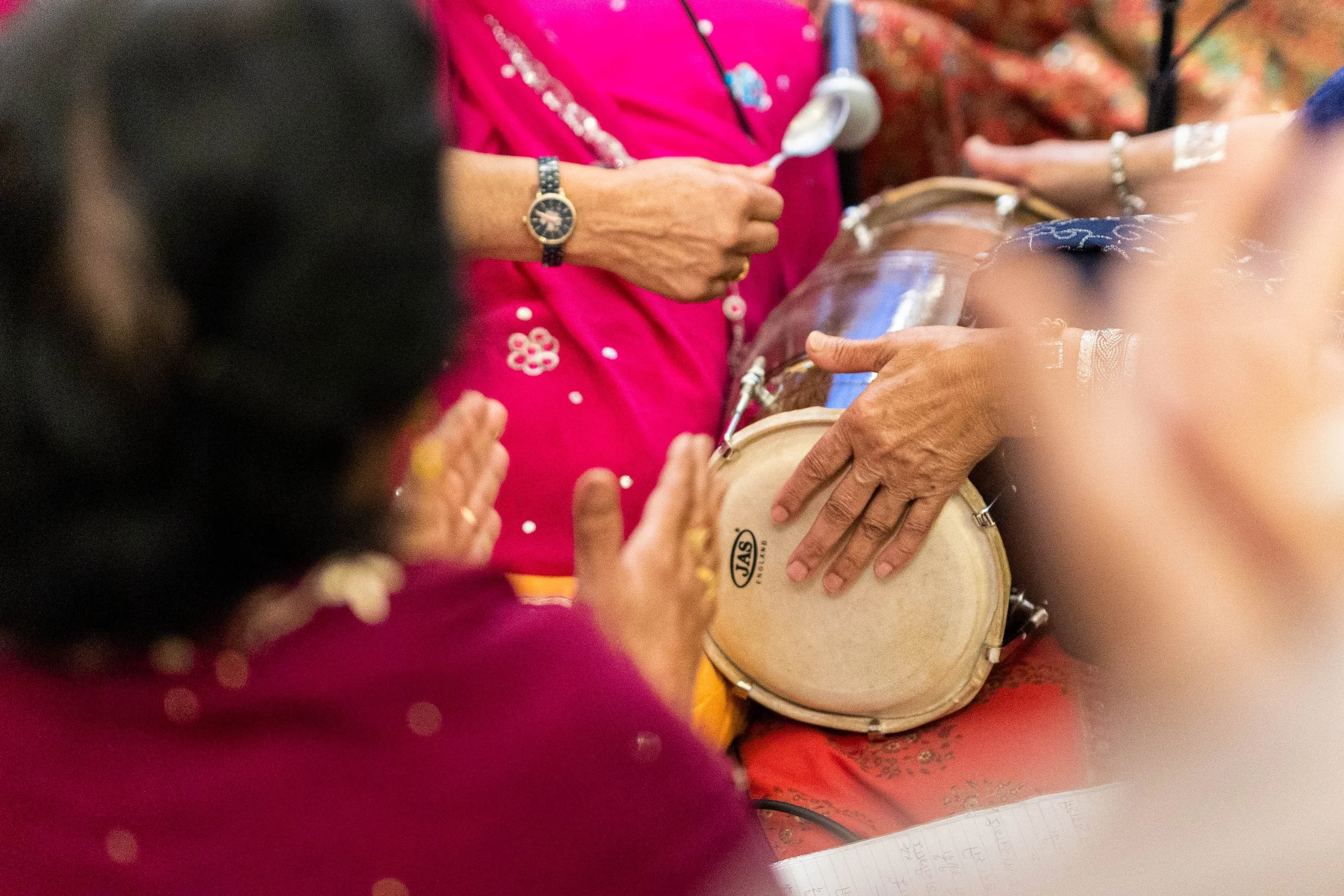 Close-up of hands playing a drum during a celebration, with several women dressed in colorful traditional clothing.