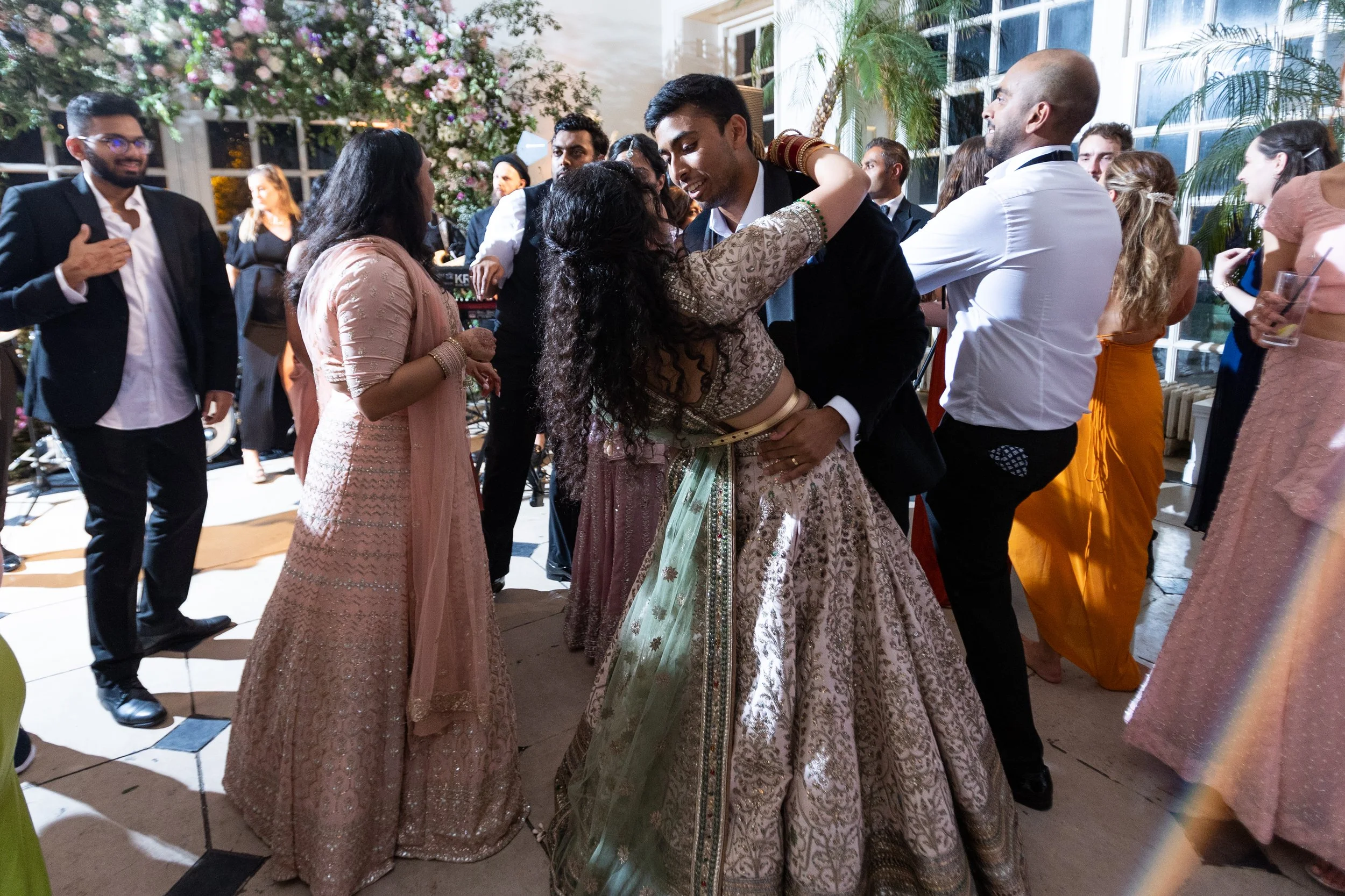 People dancing and celebrating at a wedding reception, with guests dressed in traditional Indian attire.
