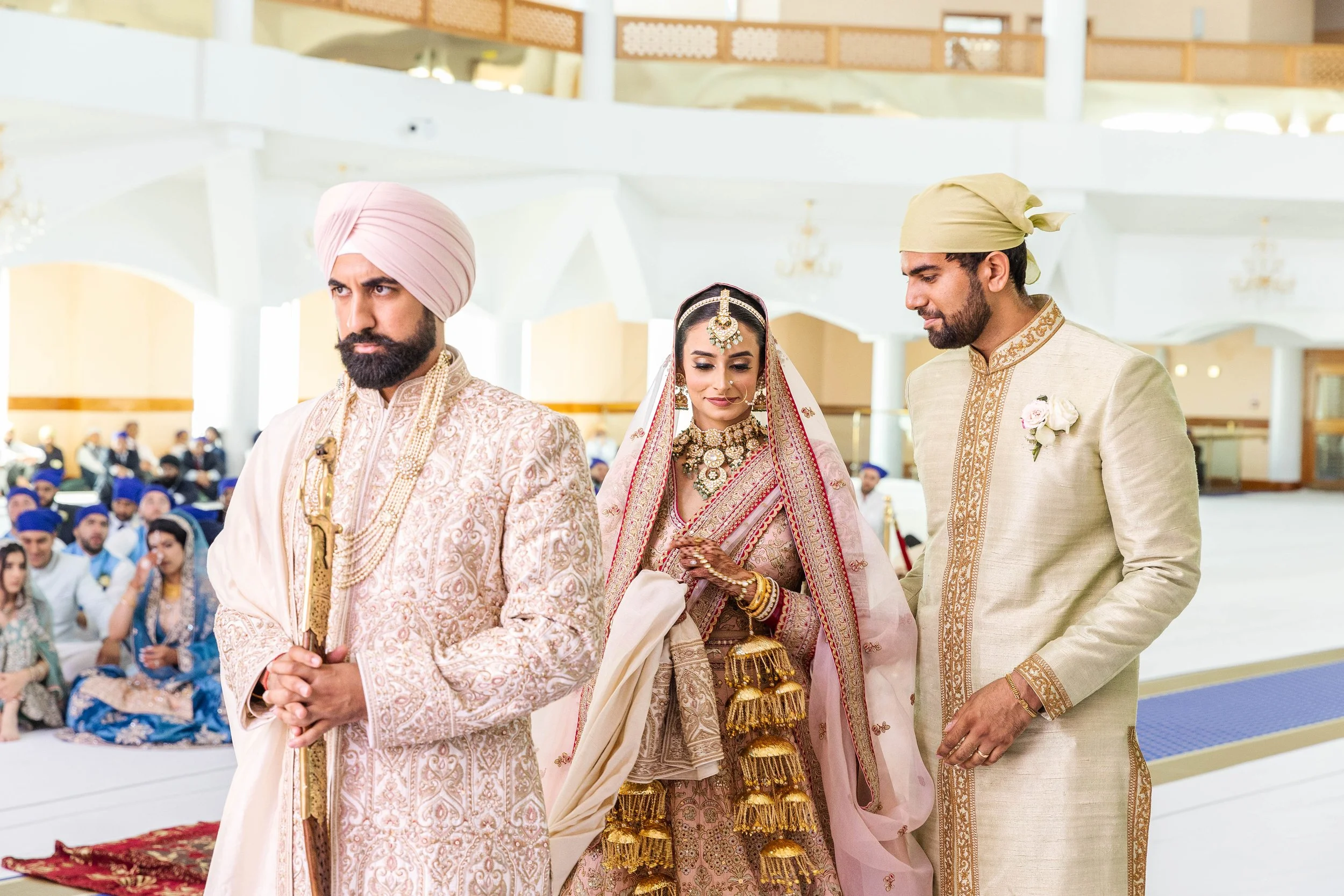 Indian wedding ceremony with bride and groom in traditional attire, officiant in front, guests seated in background