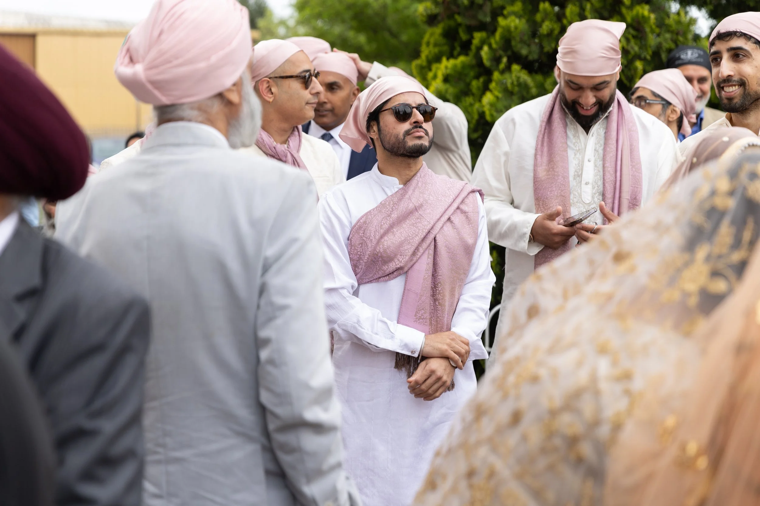 A group of men dressed in traditional Indian attire with pink turbans, gathered outdoors during the daytime.
