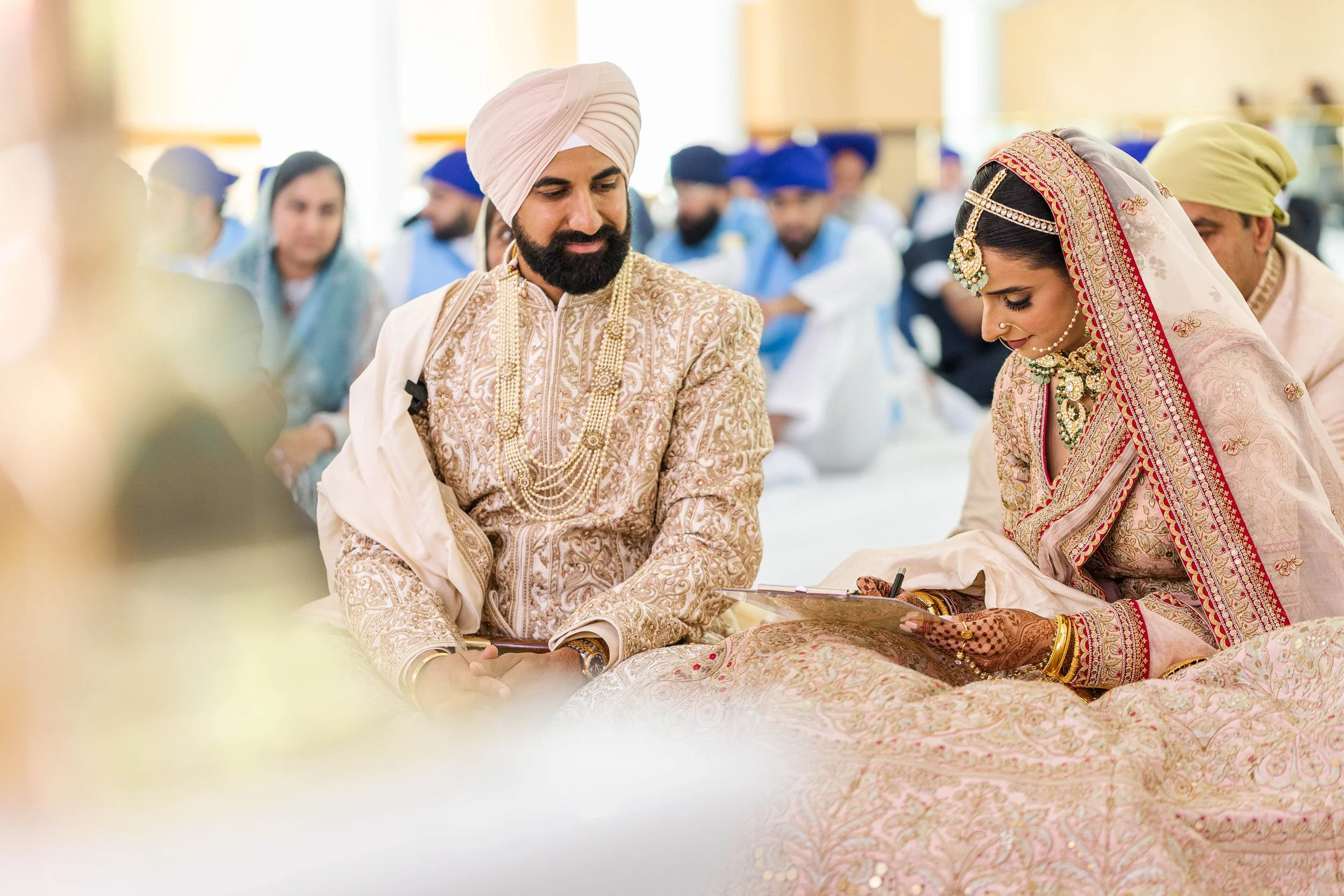 Indian bride and groom dressed in traditional wedding attire during a wedding ceremony, sitting and reading vows.