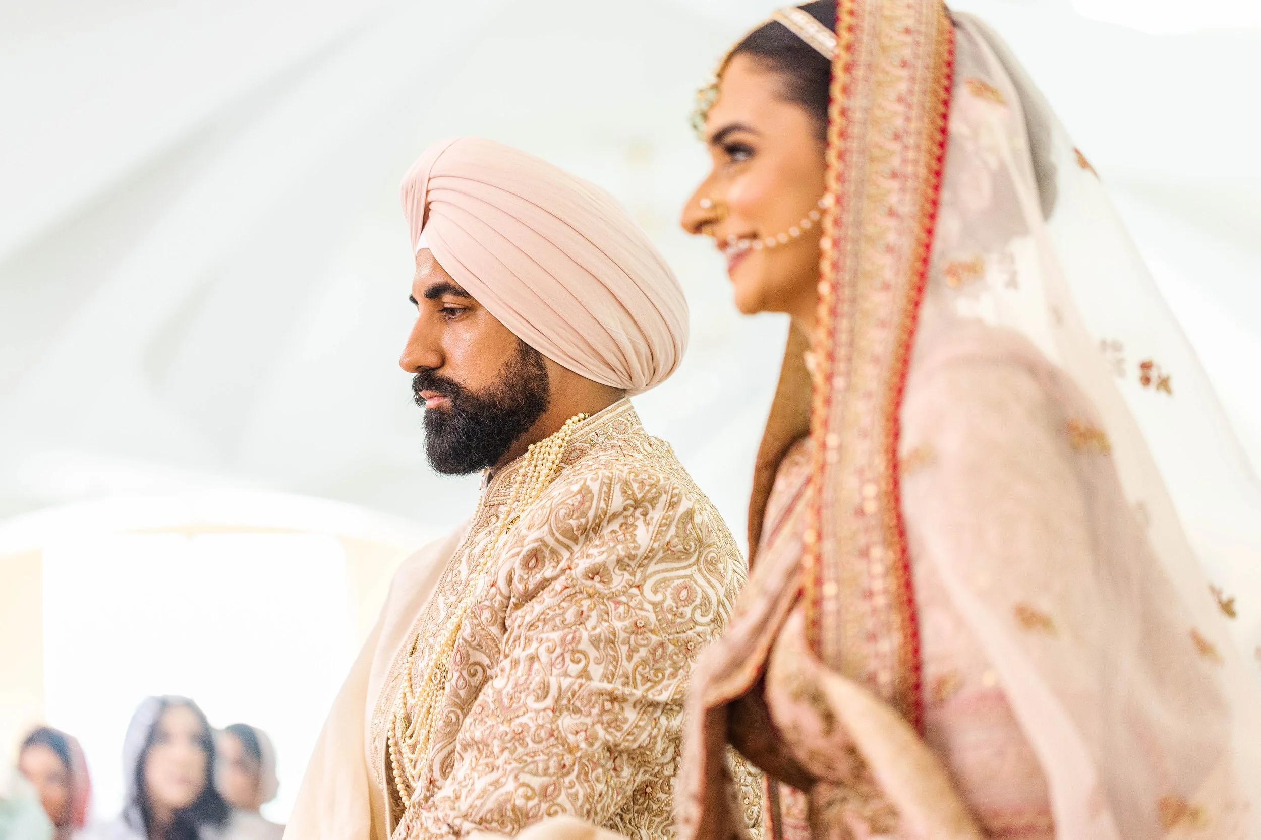 Indian bride and groom standing in a wedding ceremony, with hands joined in prayer, wearing traditional attire and jewelry.