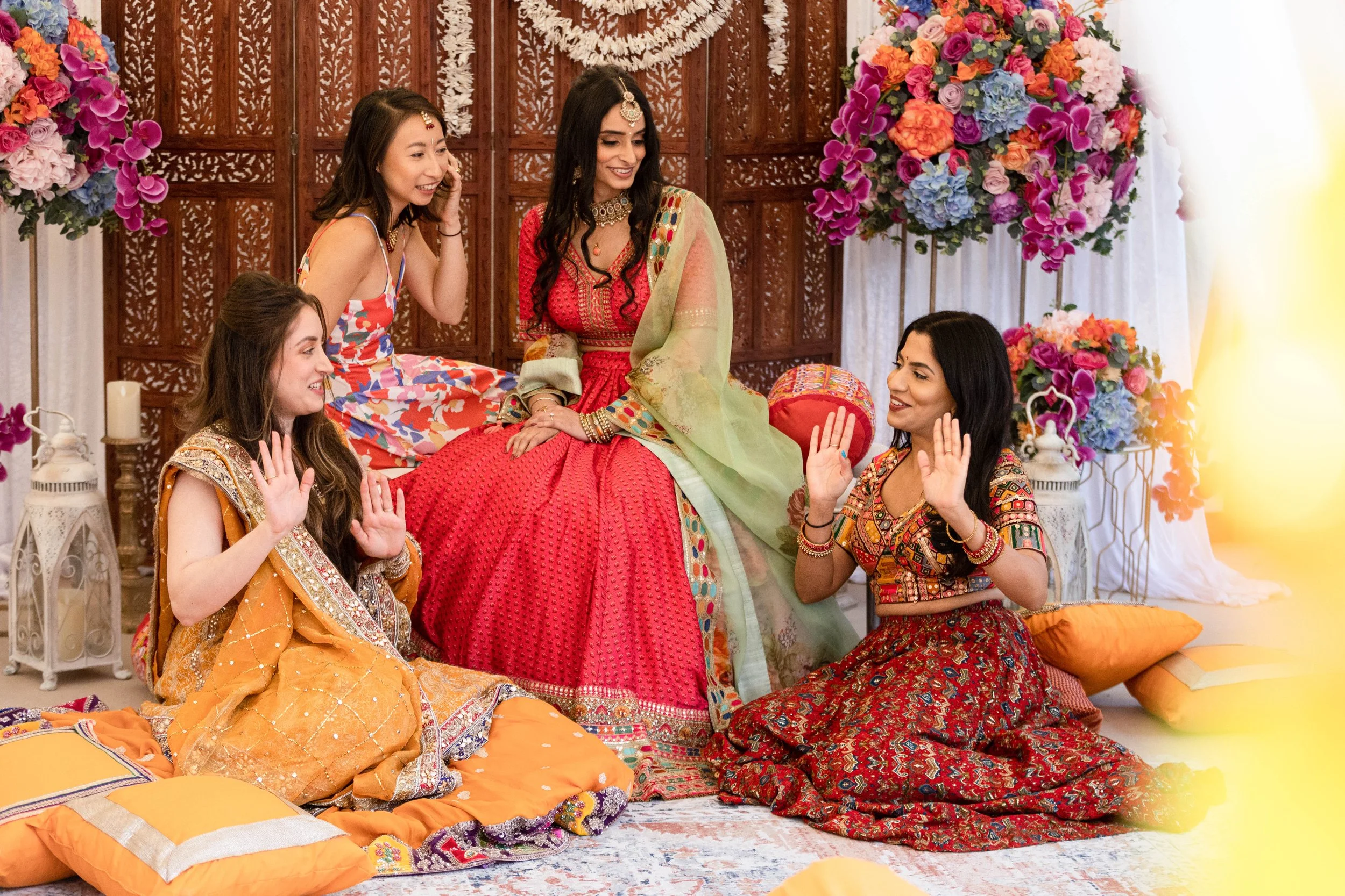Women in traditional Indian attire celebrating a cultural event with colorful flower arrangements in the background.