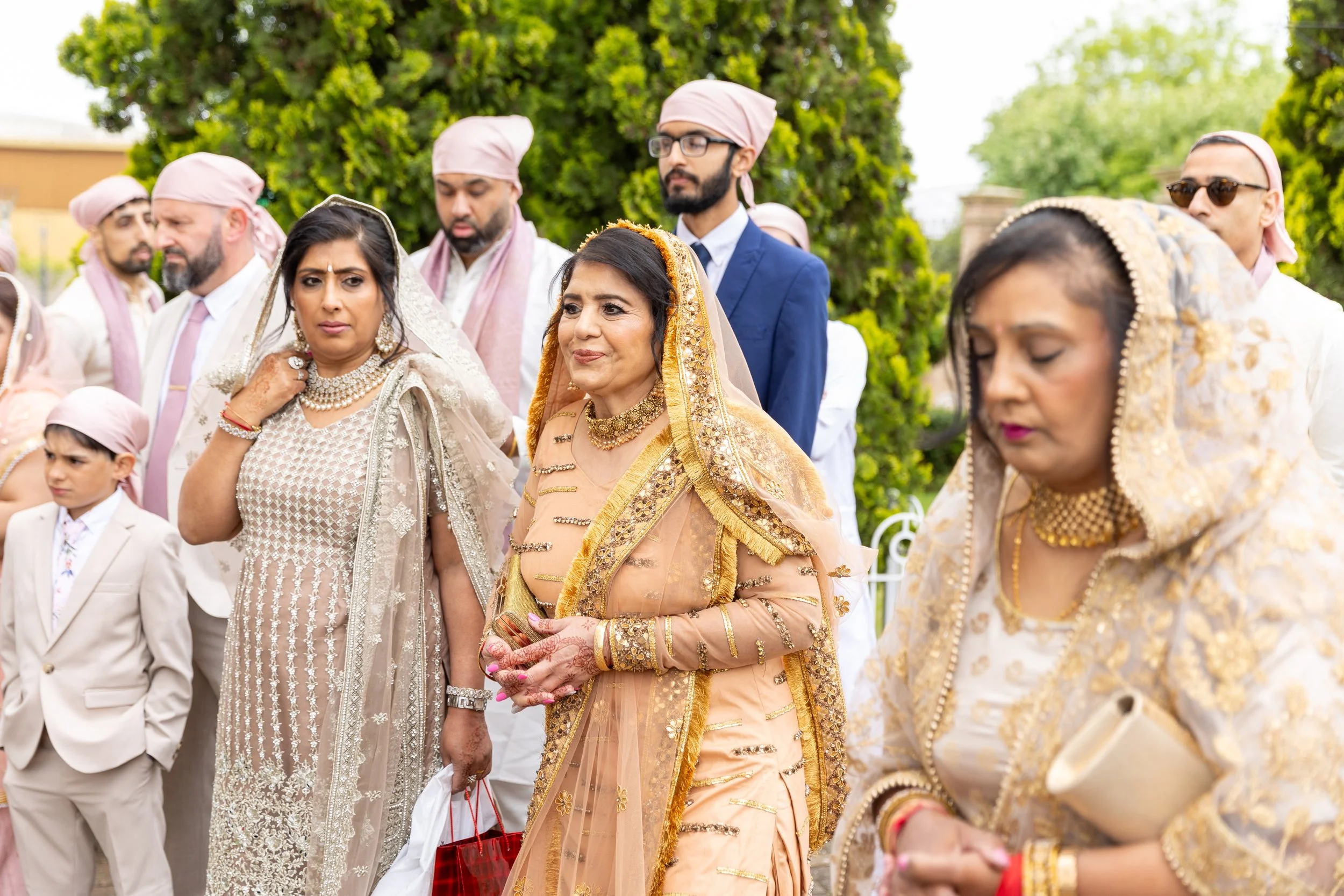 A group of people in traditional Indian attire attending a celebration outdoors, with a large green tree in the background.