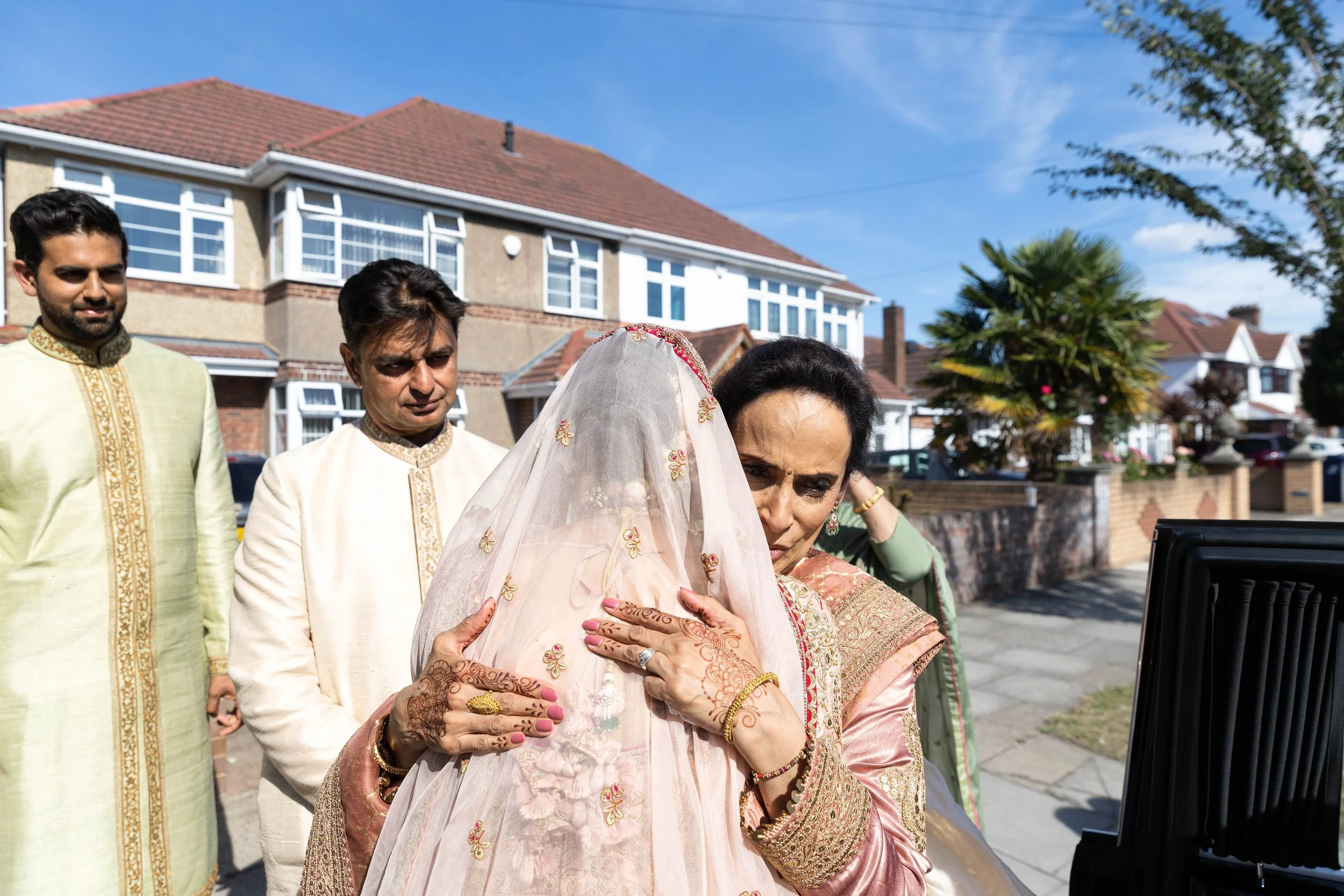 Indian woman in traditional attire comforting bride covered with a veil at an outdoor wedding ceremony.