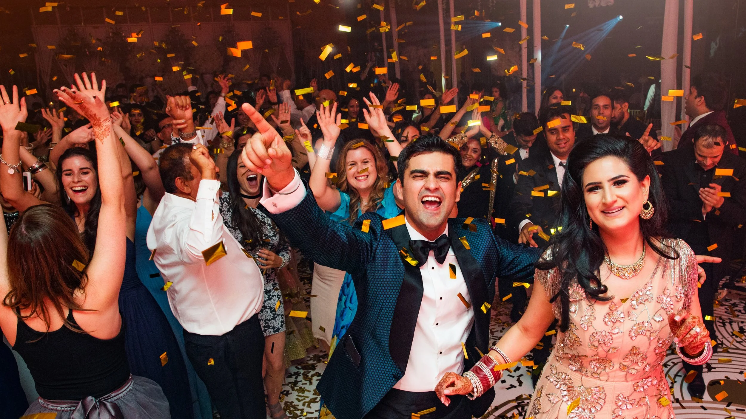 People celebrating at a party with confetti, smiling and dancing, dressed in formal attire.