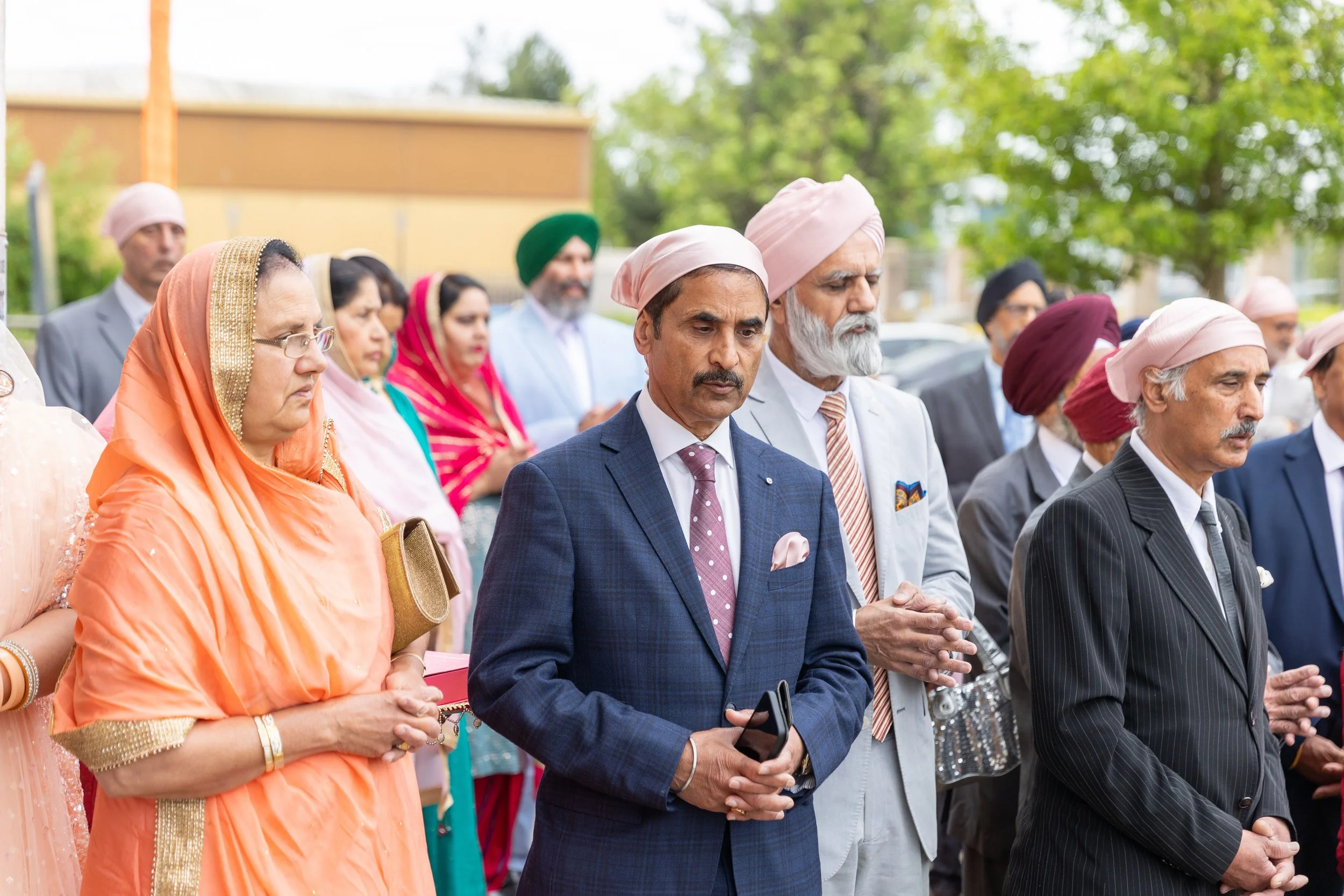 Group of people dressed in traditional Indian and Western attire participating in a prayer or religious ceremony outdoors.