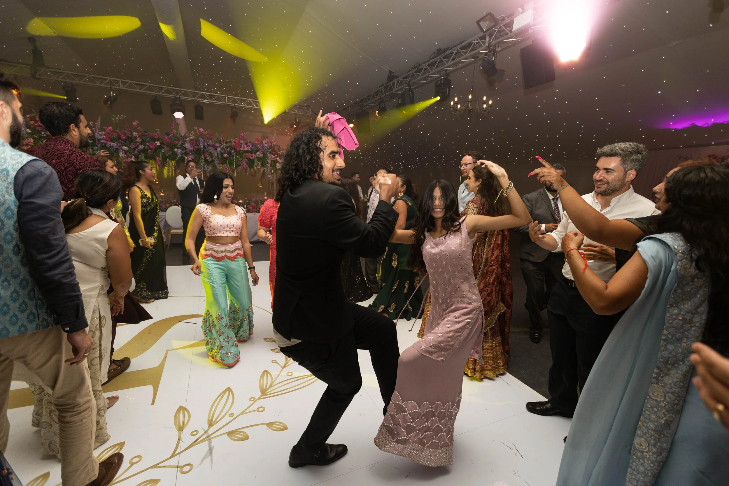 People dancing and celebrating at a wedding reception with colorful attire and festive decorations.