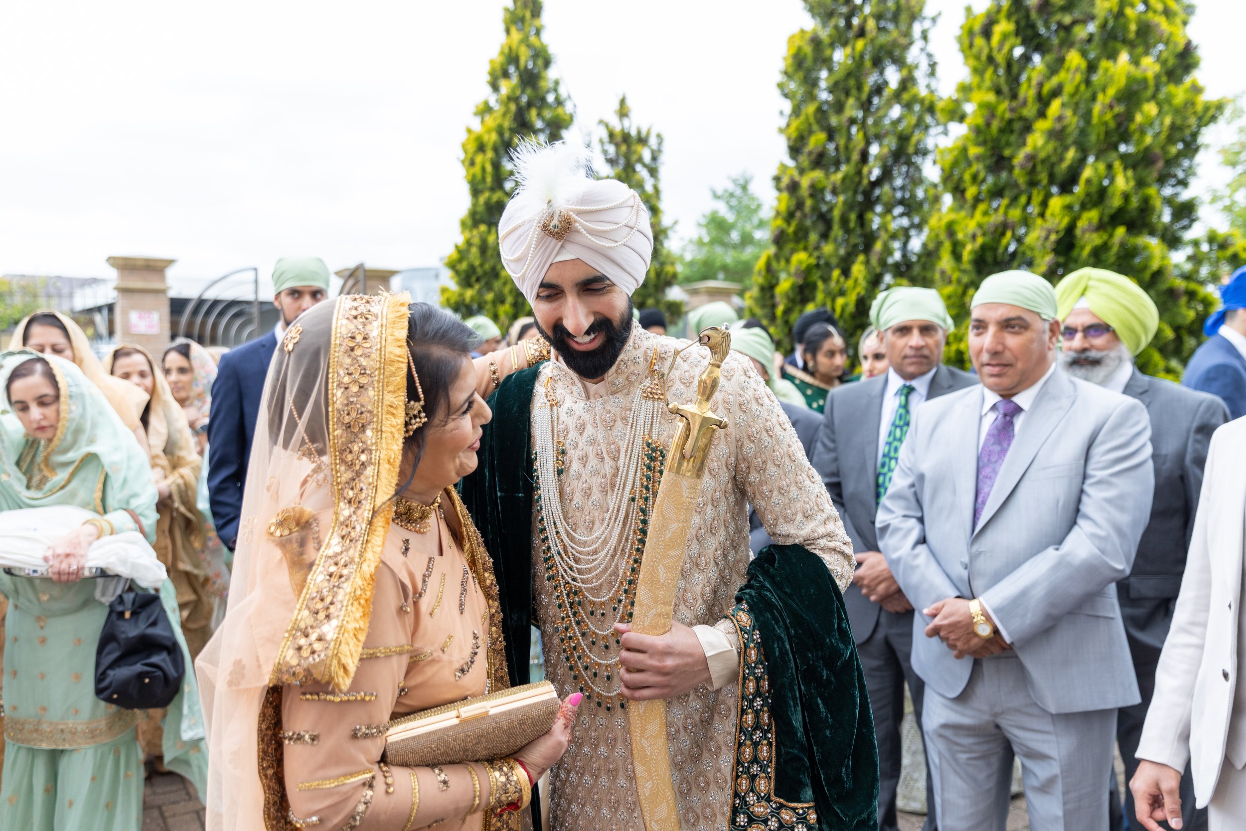 Indian groom and bride dressed in traditional wedding attire, surrounded by family and friends at an outdoor wedding celebration.