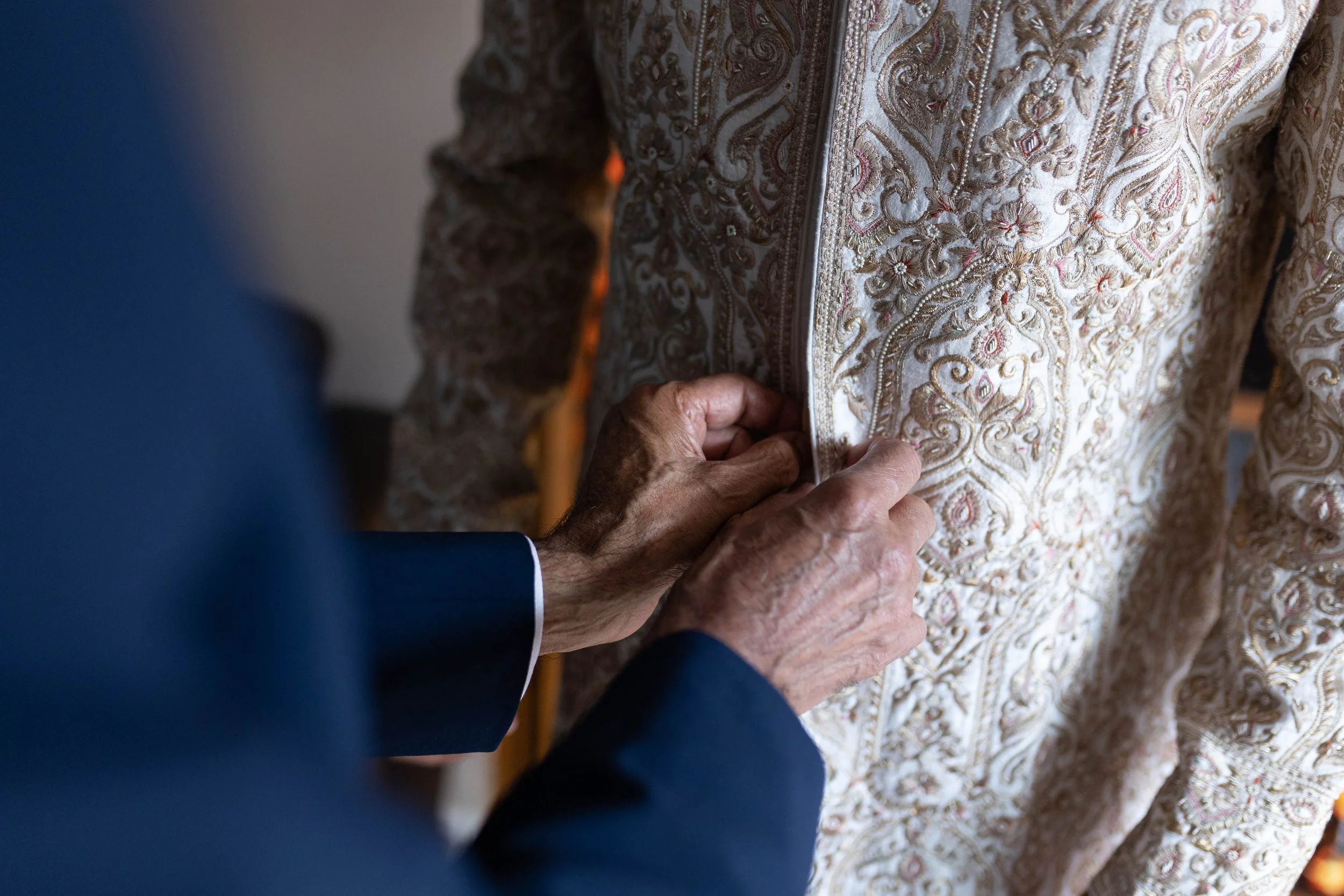 Person adjusting a traditional embroidered beige and gold jacket with detailed patterns.