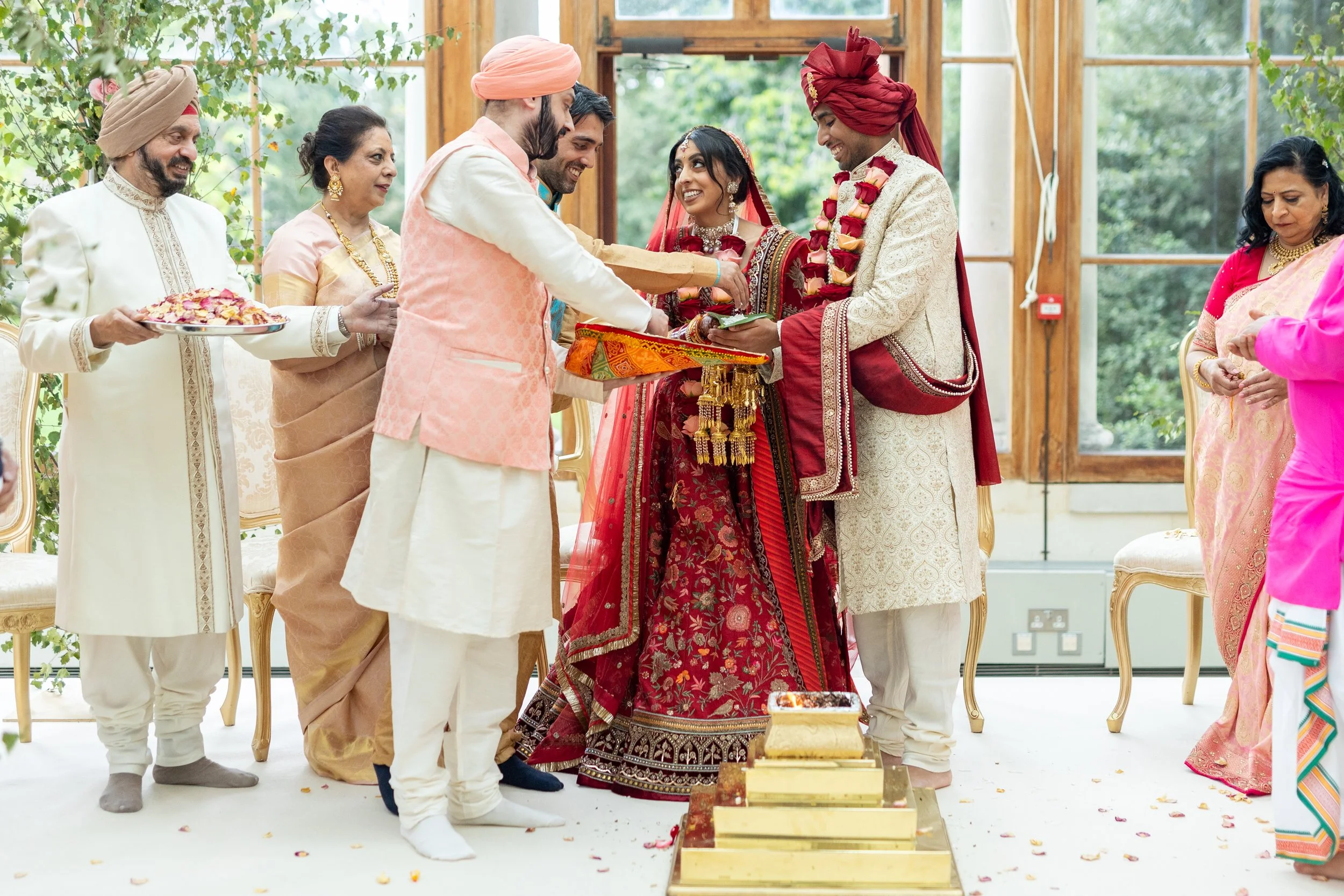 Indian wedding ceremony with bride and groom exchanging vows, surrounded by family members in traditional attire.