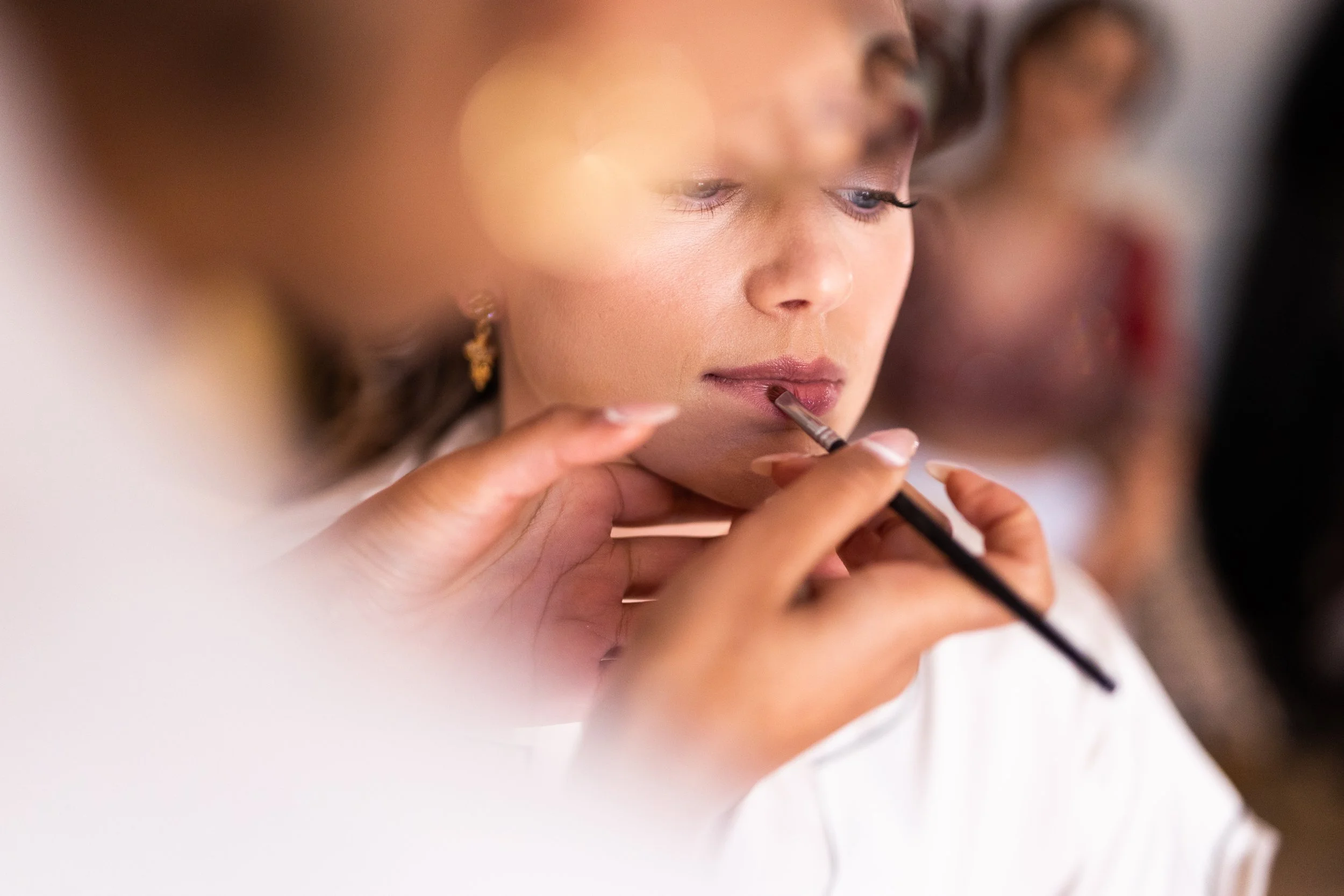 A woman getting her lips filled with lip gloss or lipstick by a makeup artist, with focus on her face and the makeup applicator.