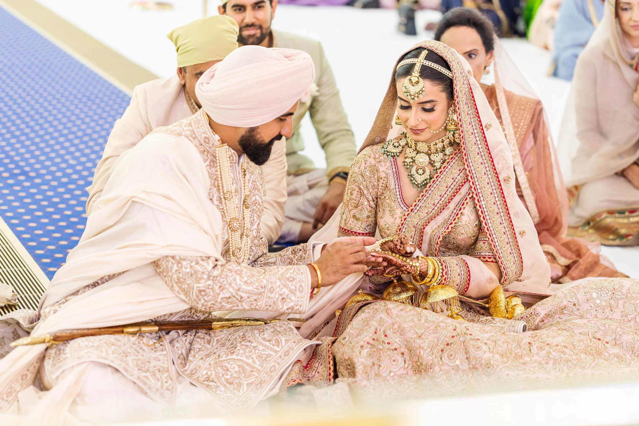Indian bride and groom exchanging wedding rings during a traditional ceremony, surrounded by family members.
