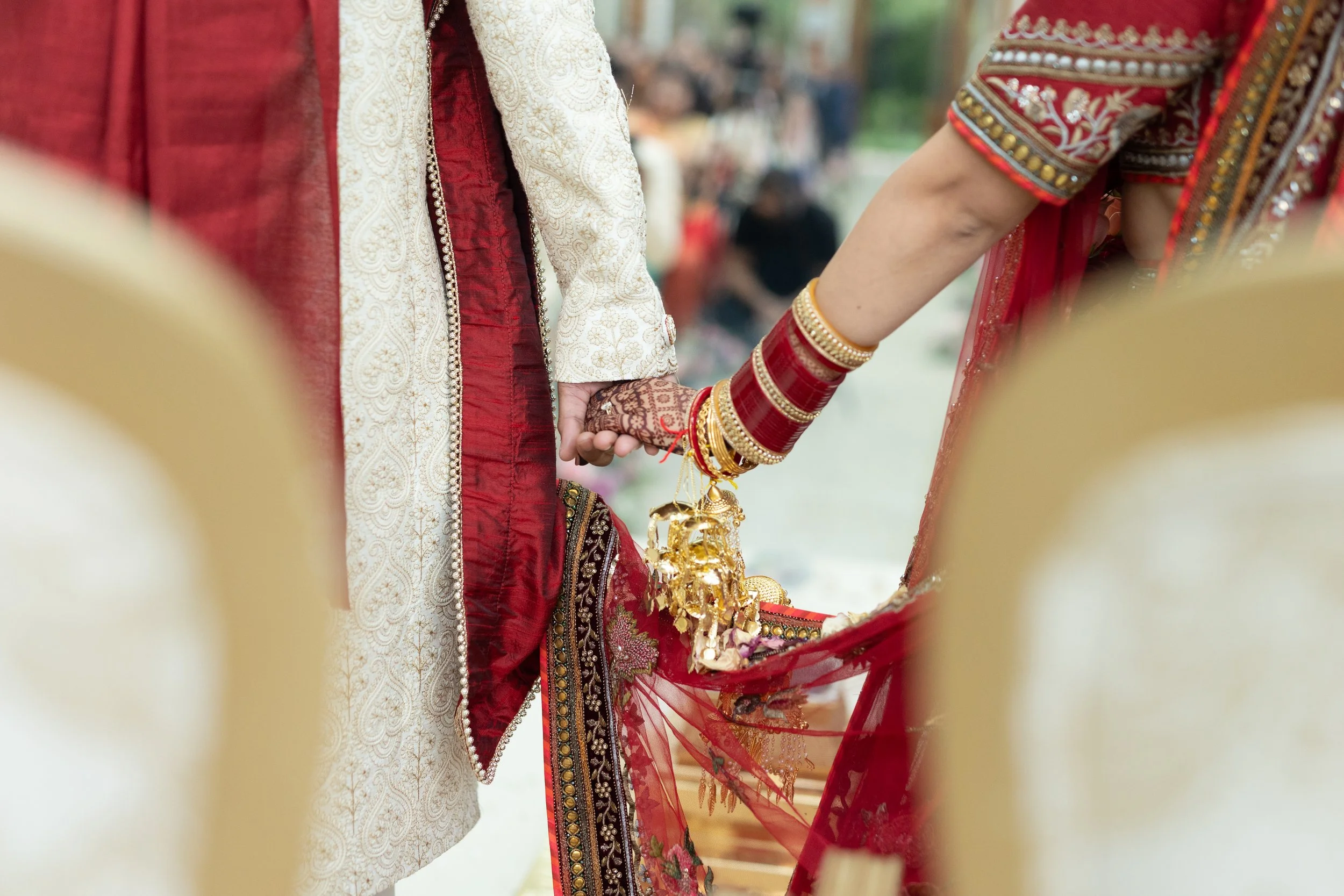 Close-up of a traditional Indian wedding ceremony, showing a bride and groom holding hands, with the bride wearing red bangles and henna on her hands, and both dressed in ornate traditional attire.