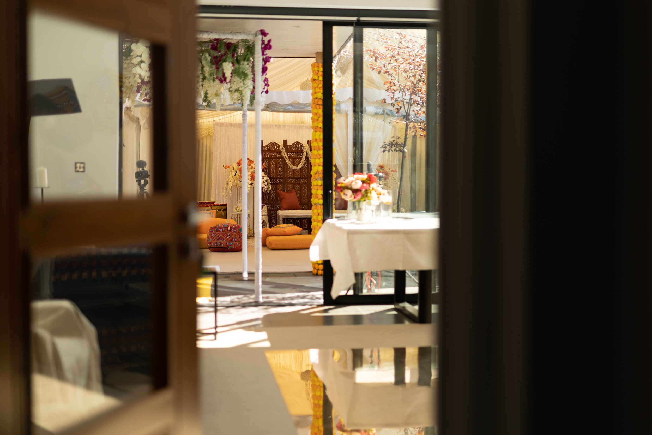 Indoor space decorated for an event with flowers, drapery, and seating area, viewed through a partially open door.