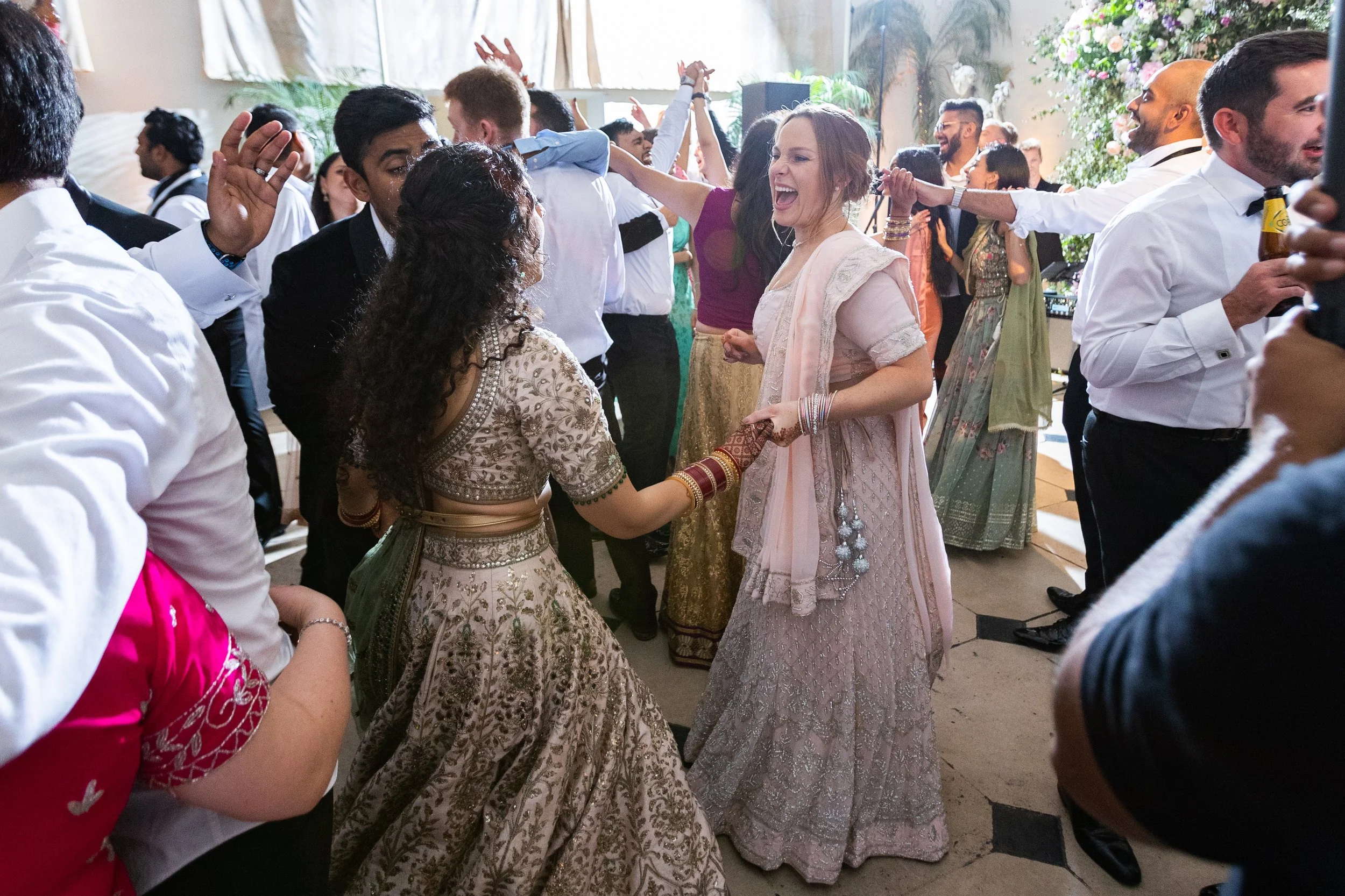 People dancing and celebrating at a wedding reception, wearing traditional Indian attire and Western formal wear.