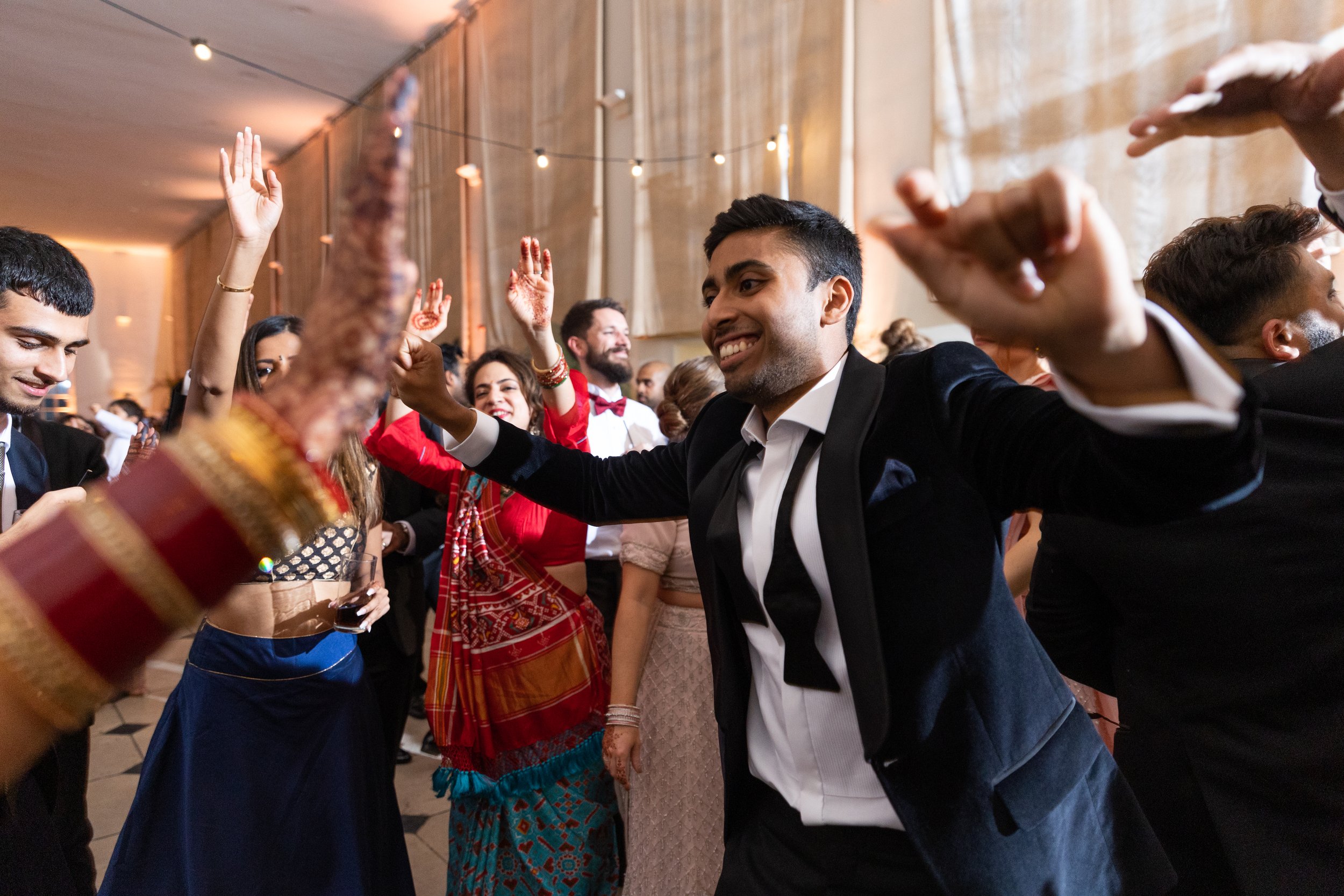 Group of people dancing and celebrating at a social event or party, some with arms raised, in a festive indoor setting.