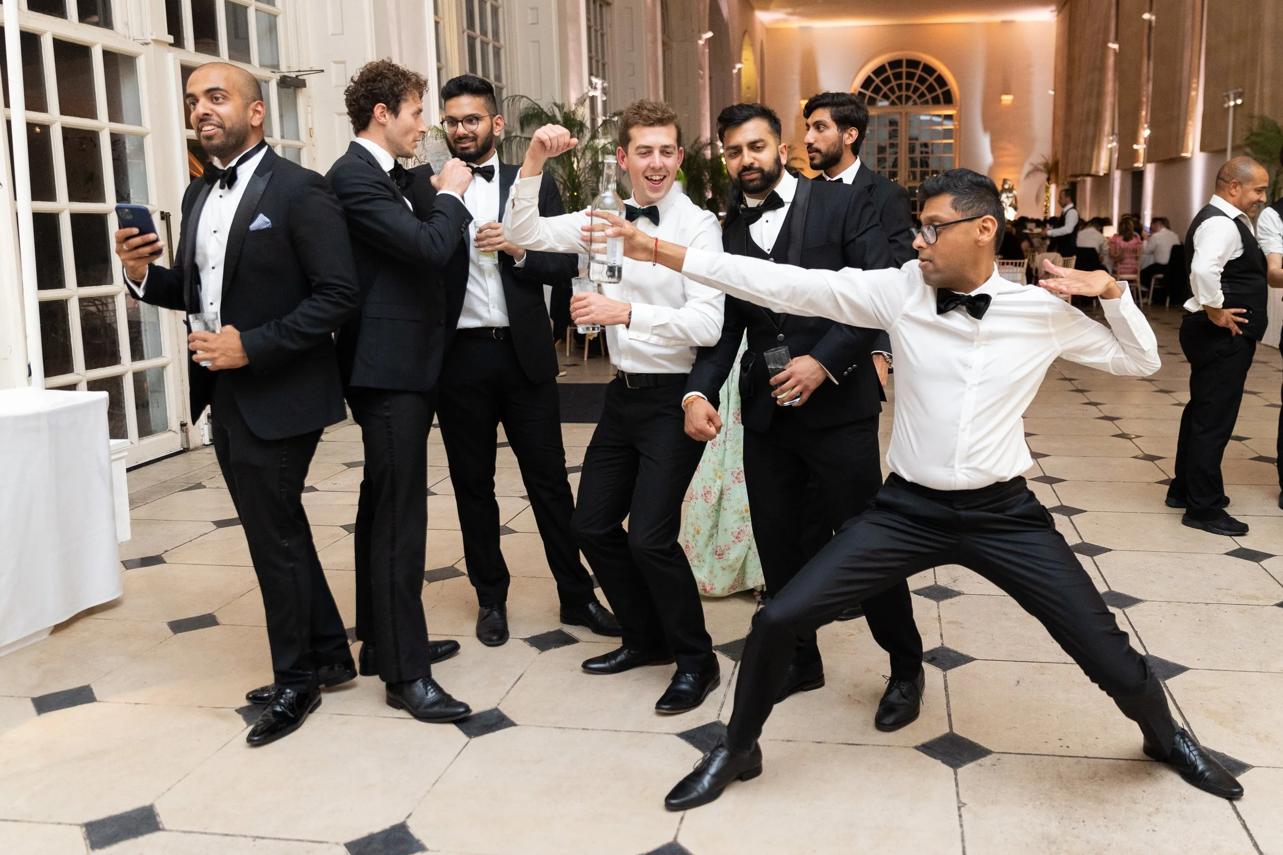 Group of men in suits dancing and celebrating at a party or wedding reception in an elegant venue.