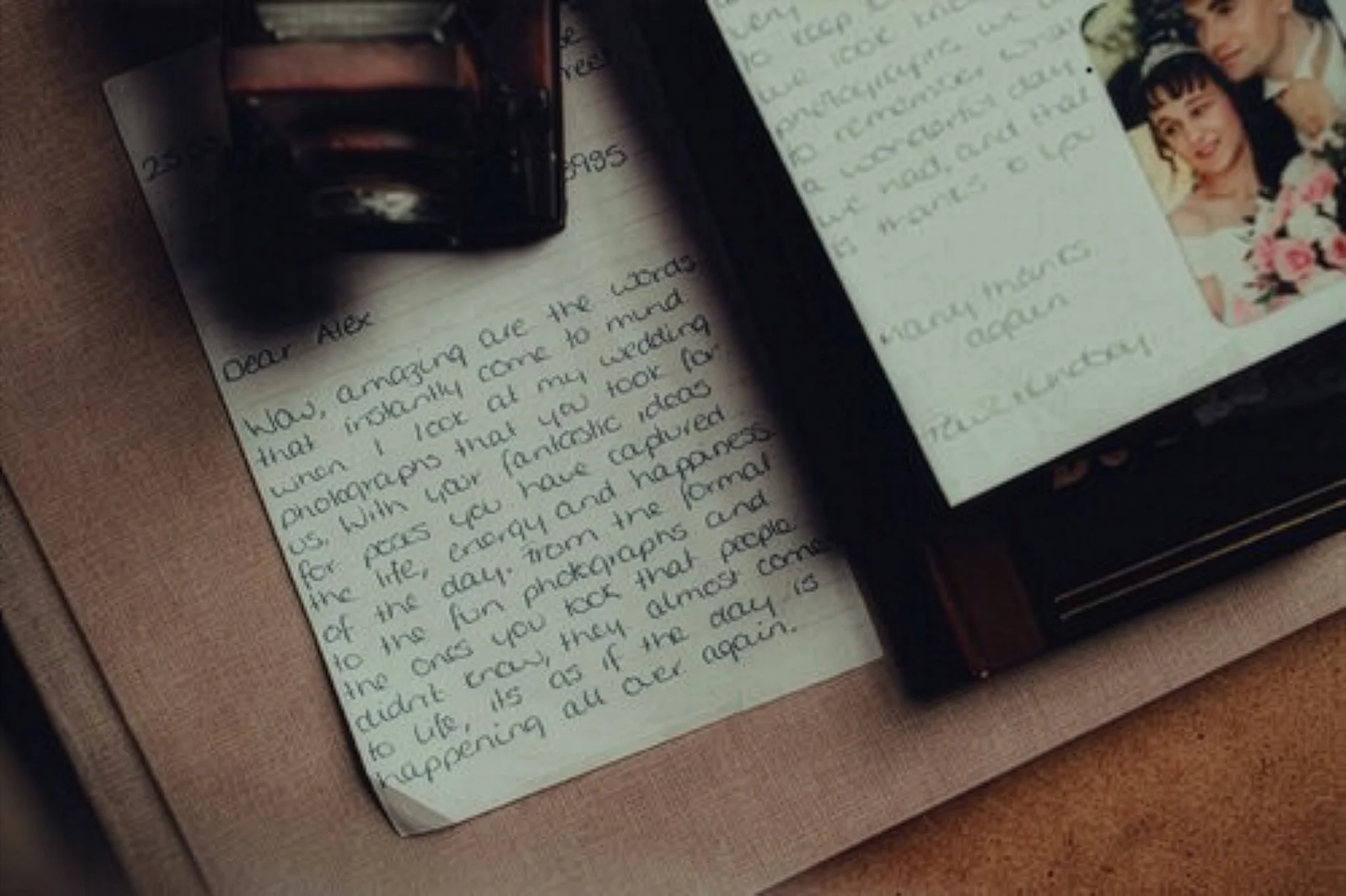 A handwritten letter on lined paper, partially covered by a small photo album with photographs. The letter starts with 'Dear Alex,' and mentions memories and photographs. A small portion of a tattooed arm is visible at the top of the image.