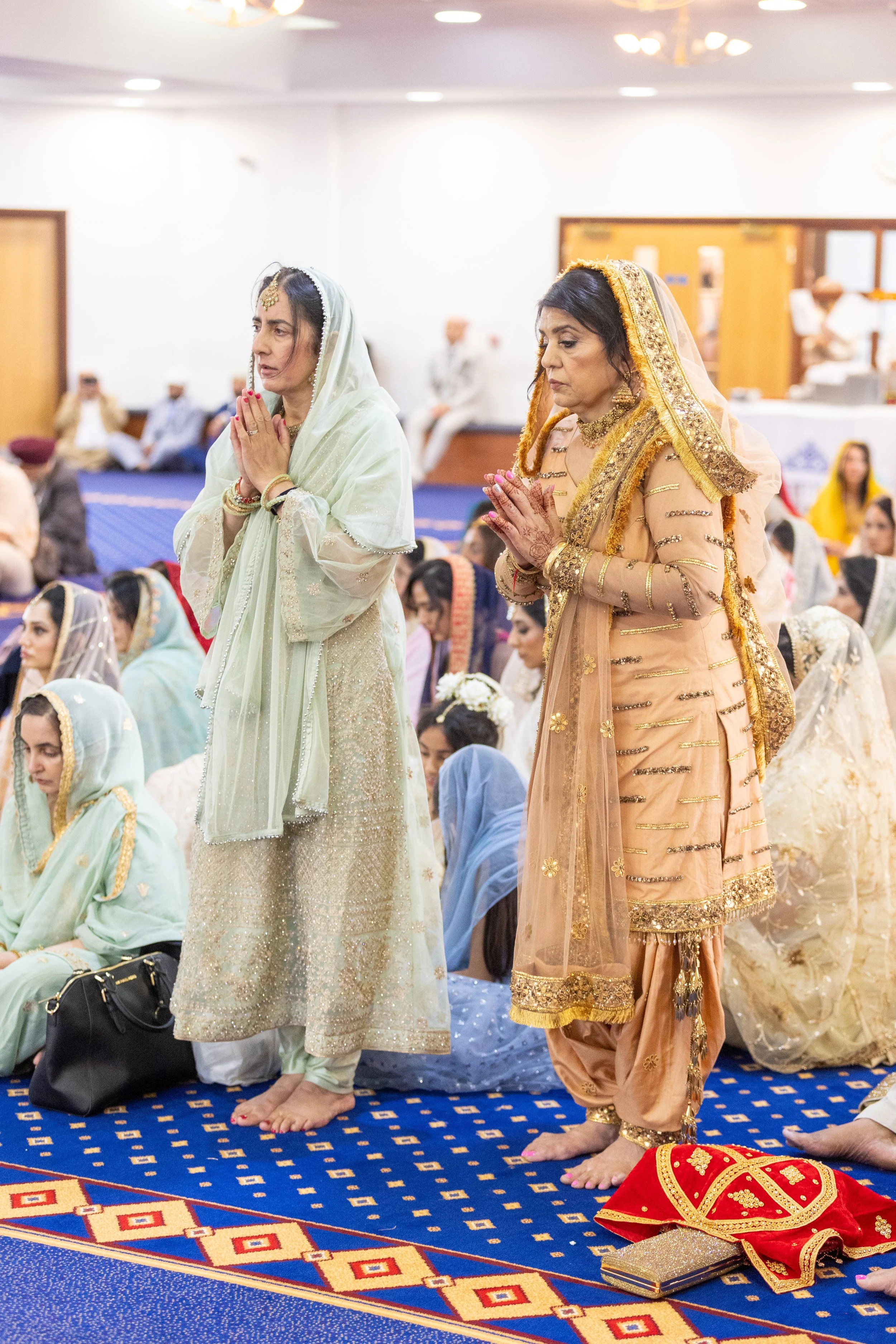 Women in traditional attire praying during a religious ceremony in a mosque.