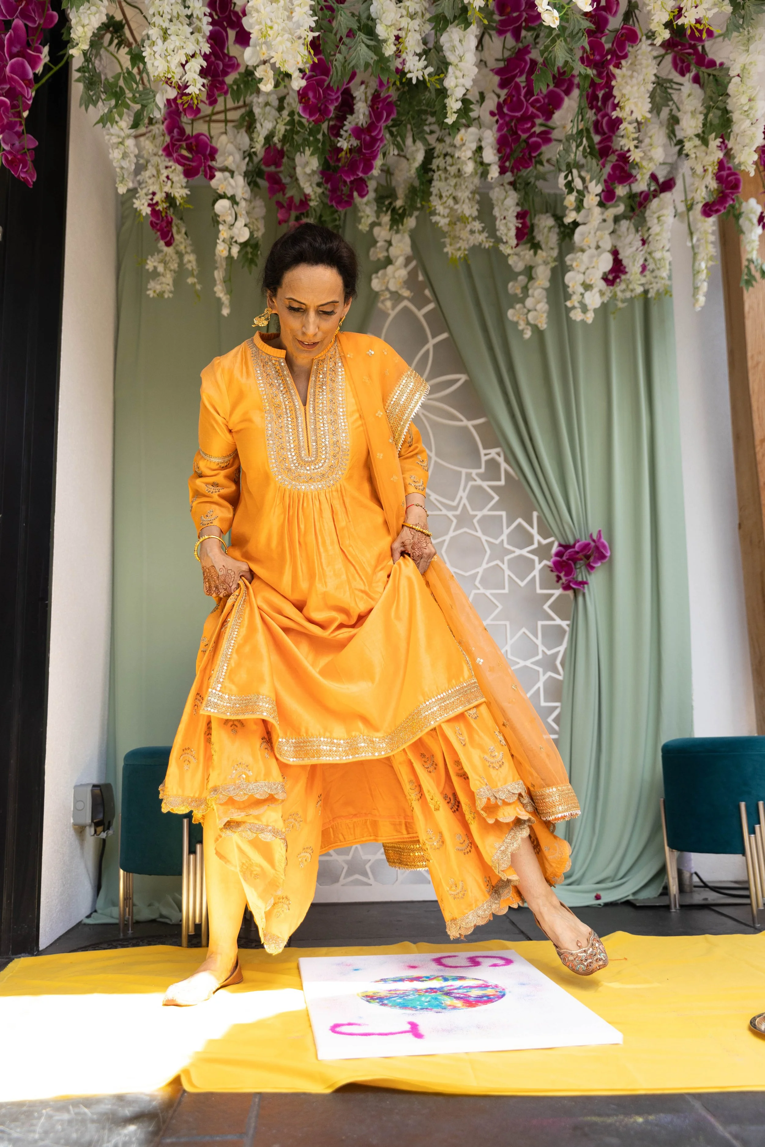 Woman in an orange traditional dress stepping on a colorful painted egg on the ground during celebration.