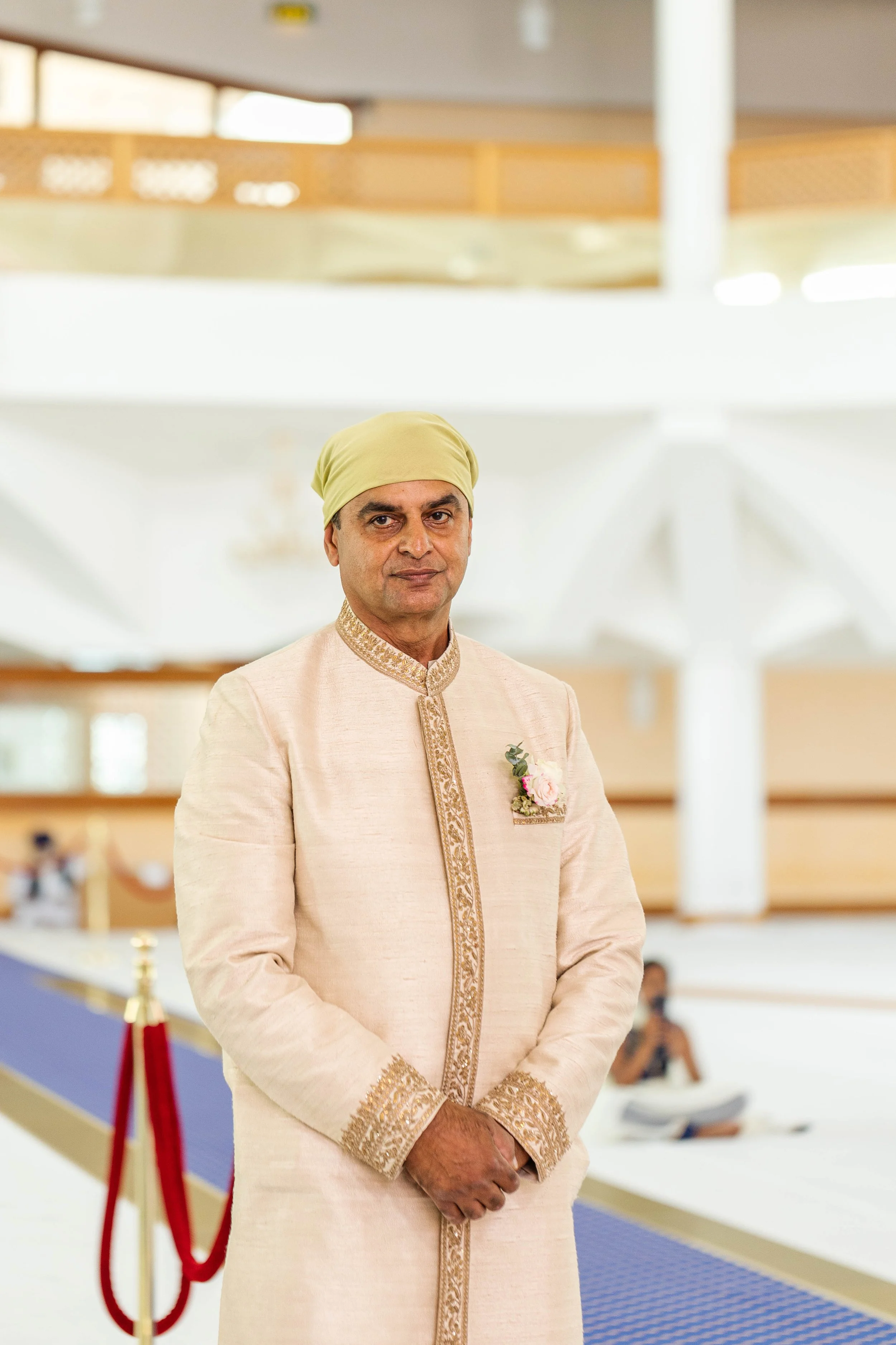 Man in traditional Indian attire standing indoors with a neutral expression.
