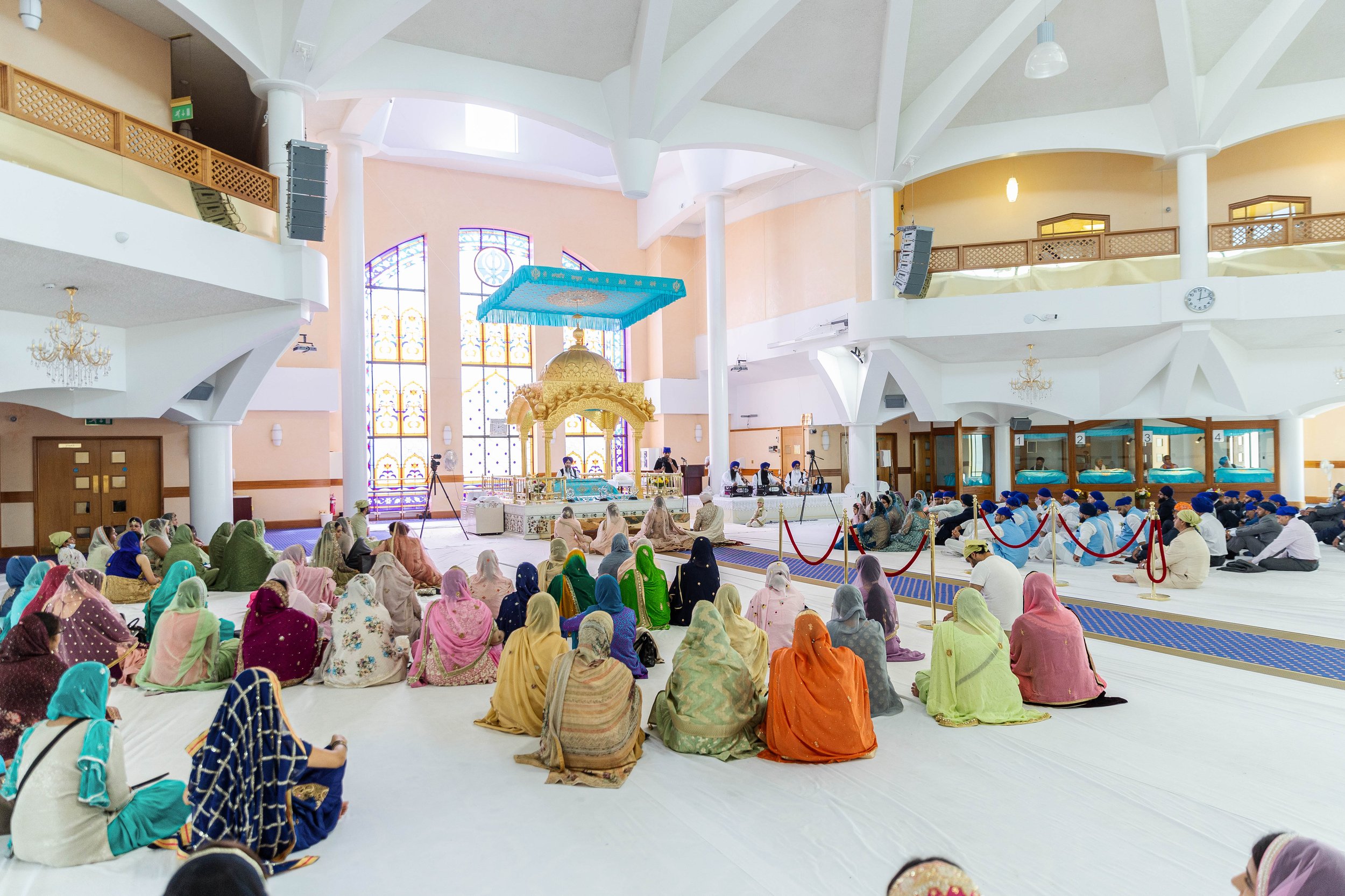 People attending a religious ceremony inside a temple with colorful stained glass windows and a golden shrine at the center.