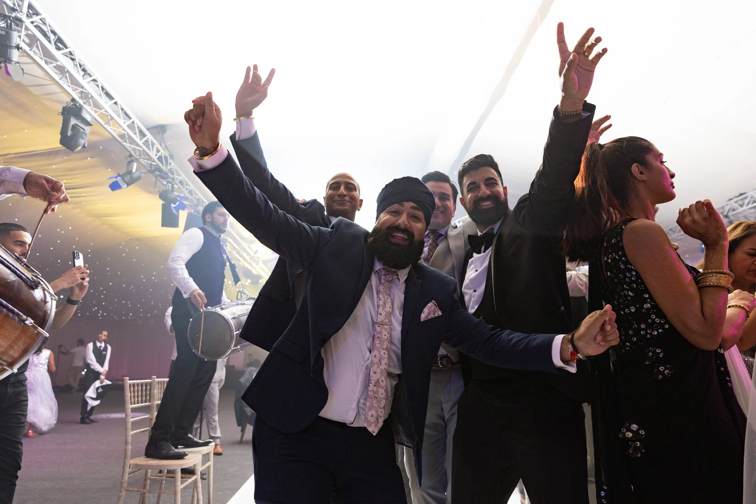 Group of people dancing and celebrating at a lively event or party with stage lights and musical instruments in the background.