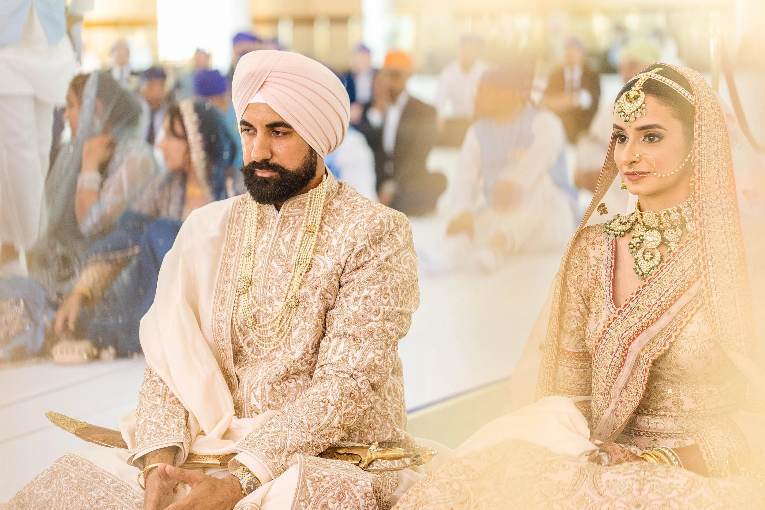 Man and woman dressed in traditional Indian wedding attire, sitting during a wedding ceremony.