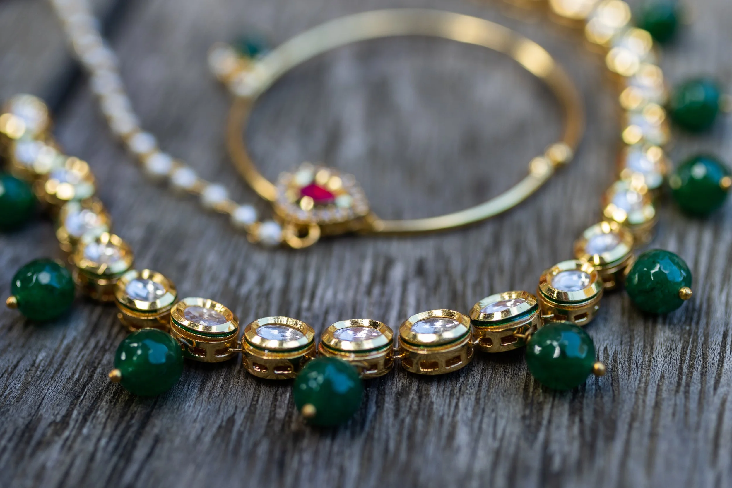 Close-up of a gold and gemstone necklace with green beads and clear stones on a wooden surface.