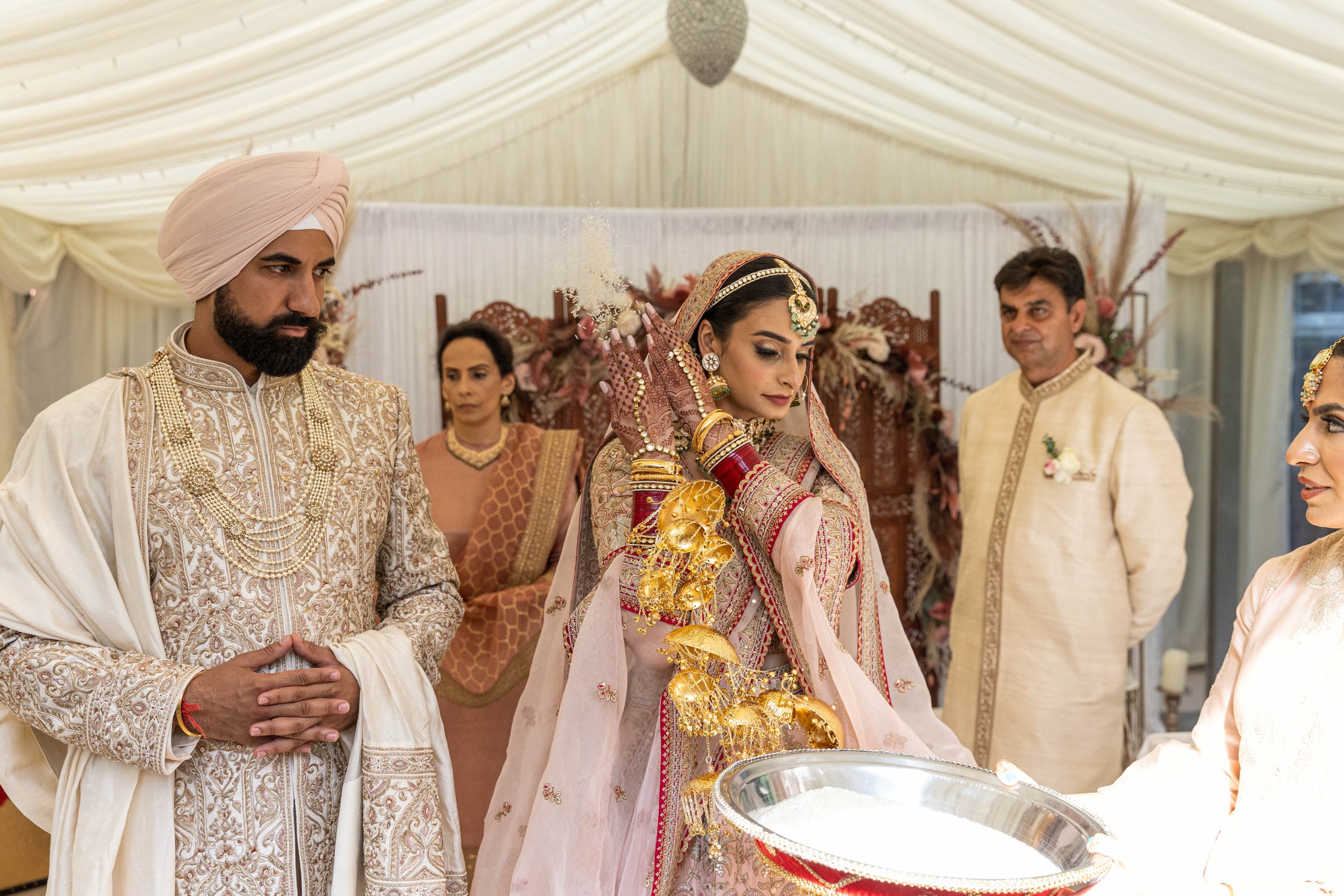 Indian bride and groom in traditional wedding attire participating in a ceremony with family members in a decorated group setting.