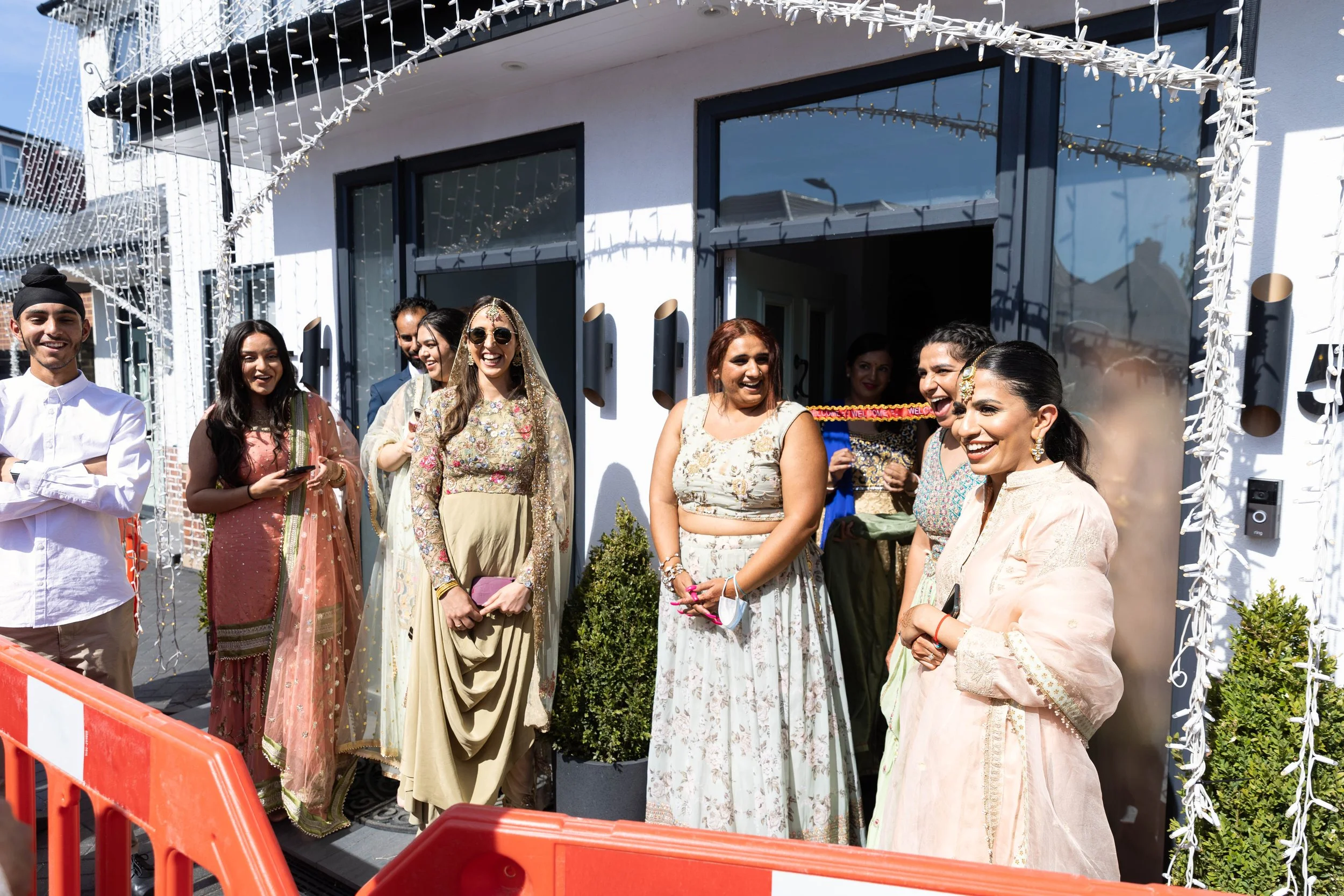 Group of people standing outside a building, celebrating a festive occasion. They are dressed in traditional and festive clothing, smiling, and enjoying the event.