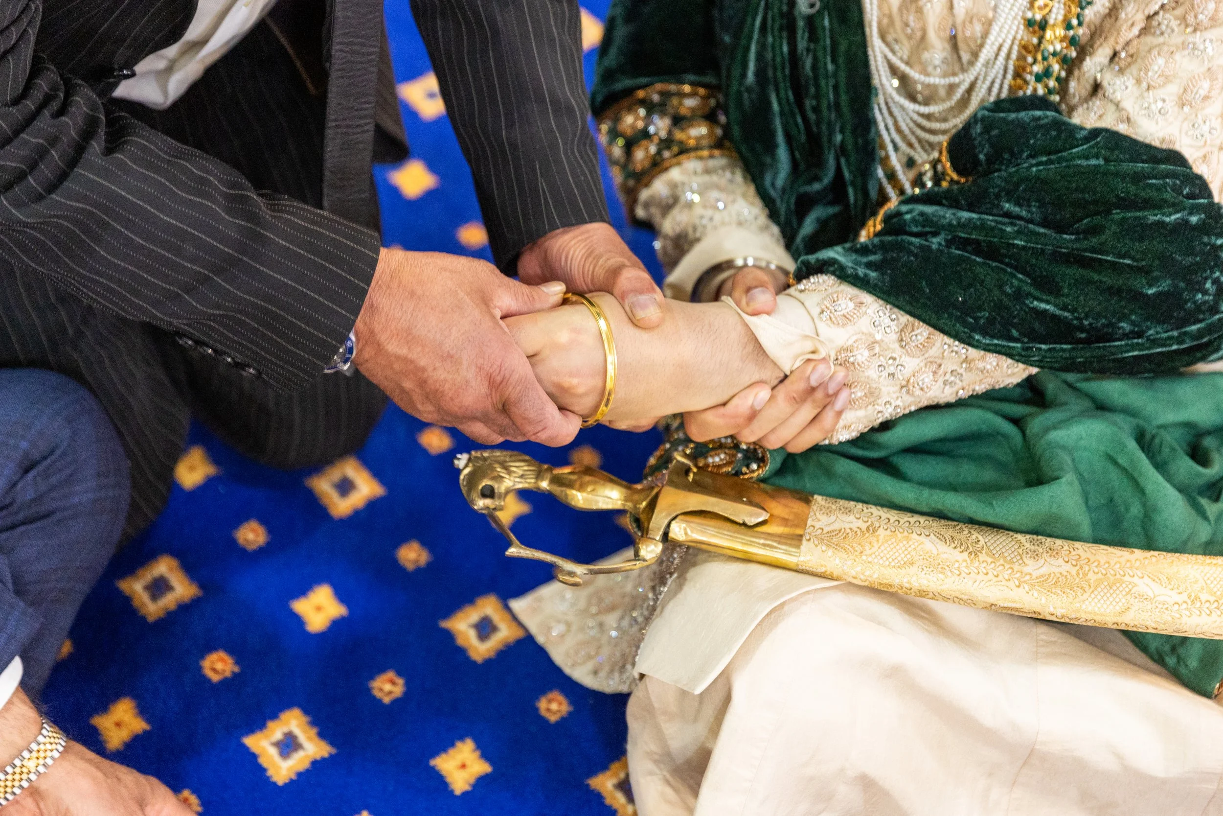 A close-up of a handshake between two people, one wearing a striped suit and the other in traditional attire, with a decorative sword placed nearby.