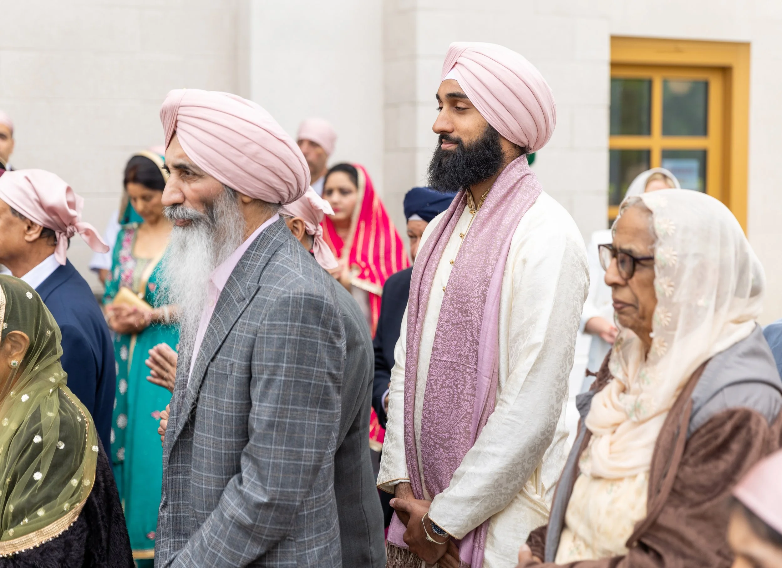 A group of people dressed in traditional Sikh attire, including turbans and headscarves, attending a ceremony outside.