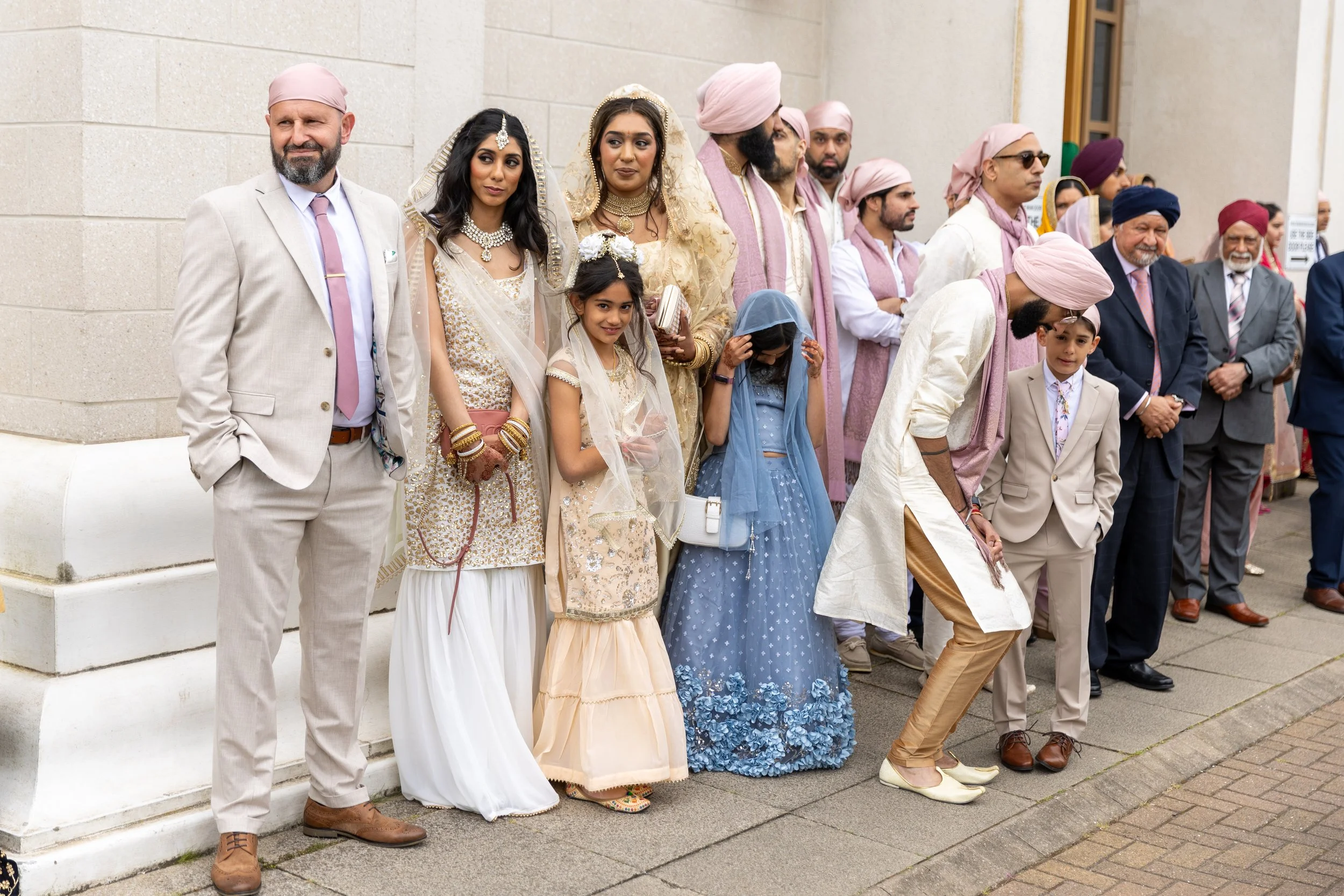 Group of people attending a cultural or religious event outside, dressed in traditional Sikh and Indian attire, some bowing or adjusting clothing.