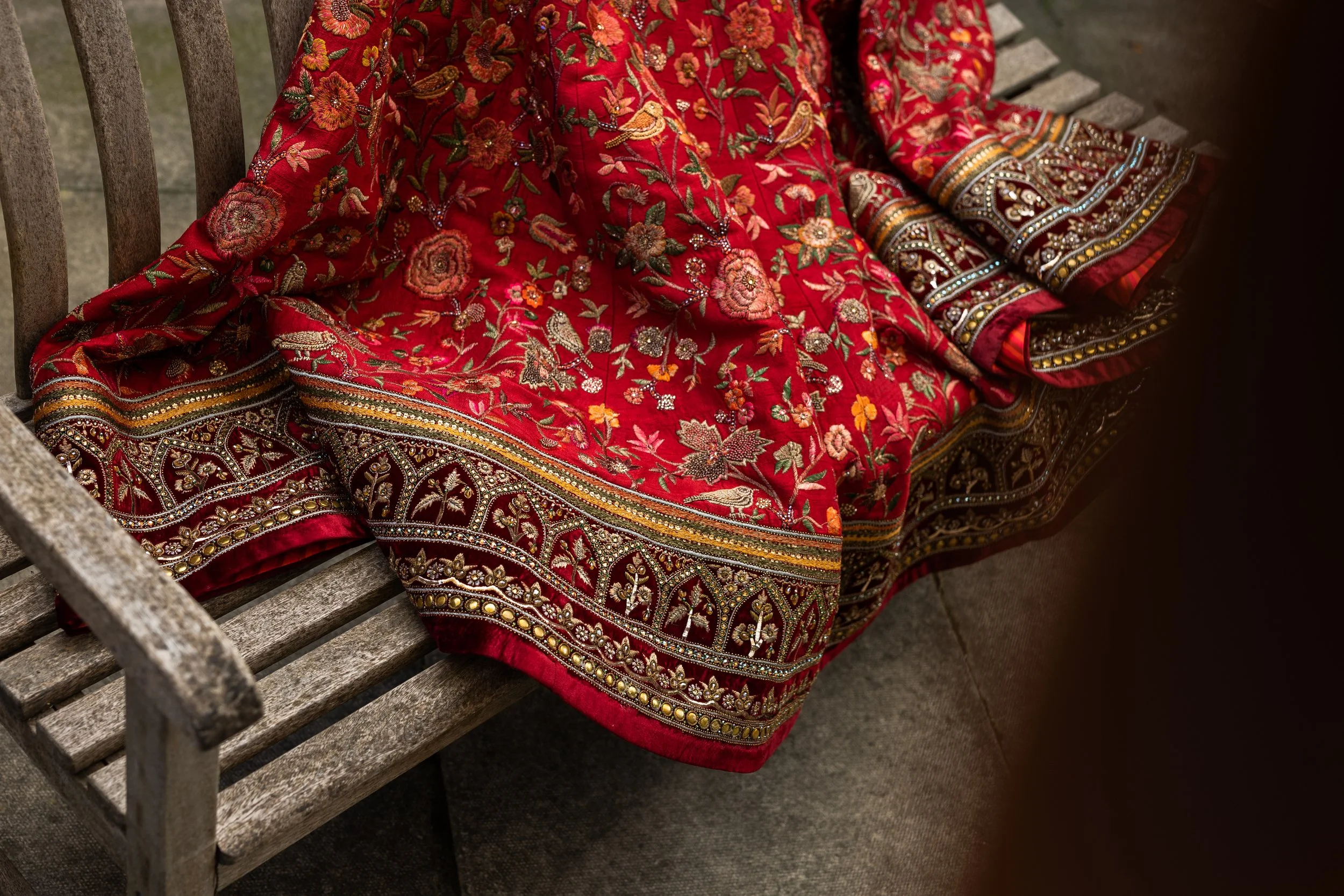 Close-up of a richly embroidered red traditional embroidered dress with intricate floral and bird patterns, draped over a weathered wooden bench.