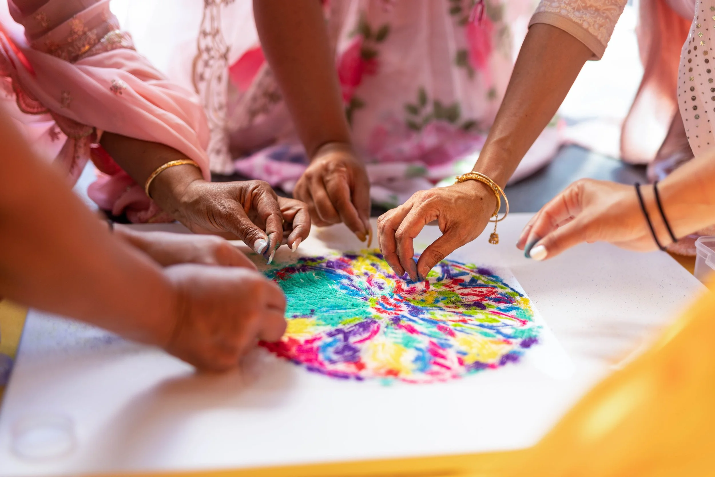 Multiple people working together to create a colorful, circular art piece on paper using tie-dye or similar fabric dyeing technique.