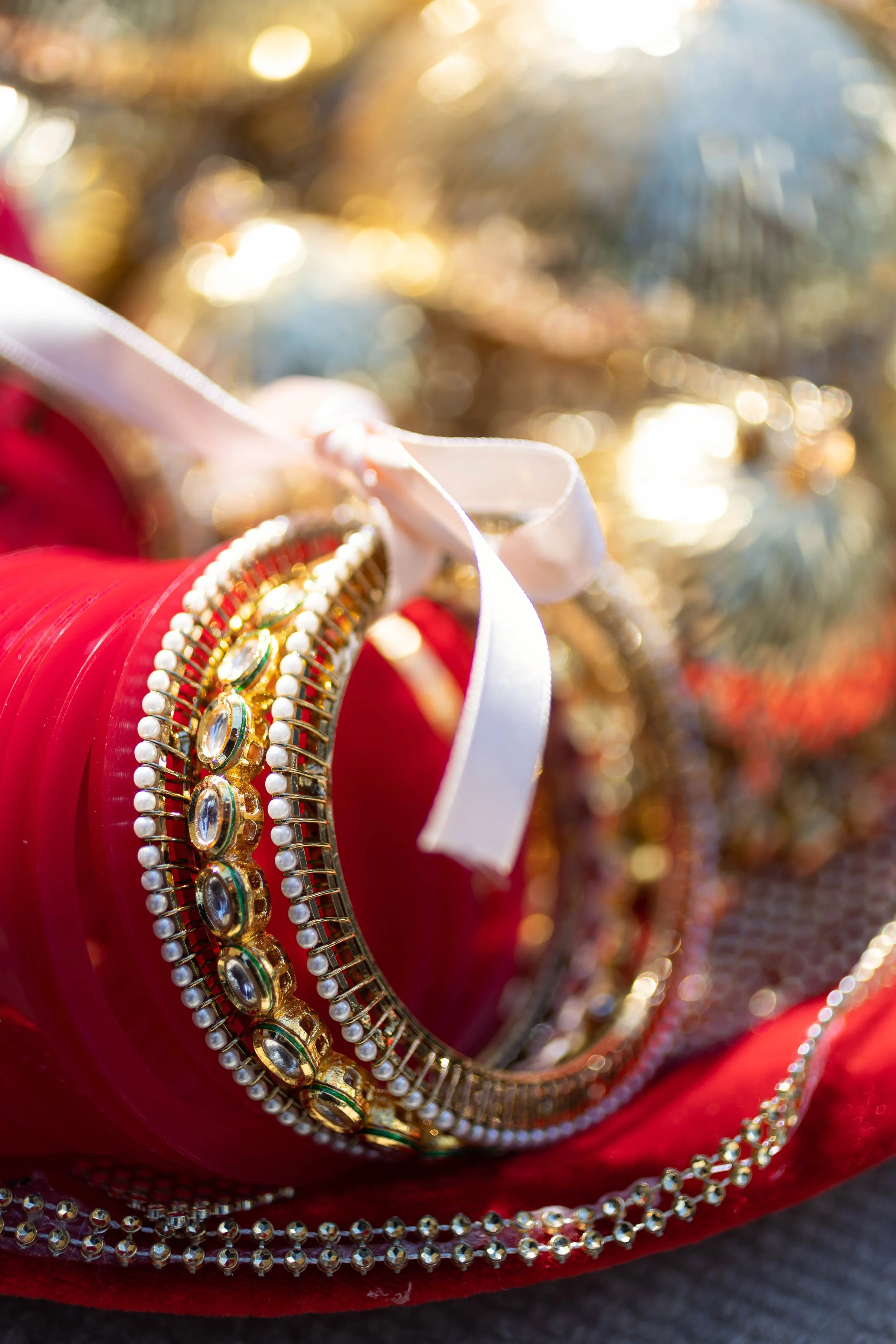 Gold and silver jewelry with gemstones, featuring a bracelet and a necklace, resting on red velvet fabric with blurred gold and green ornaments in the background.
