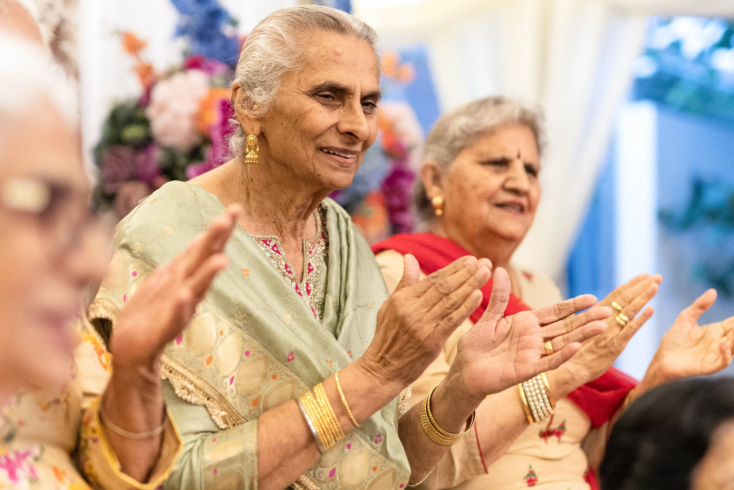 Elderly women in traditional Indian attire celebrating together, clapping their hands.