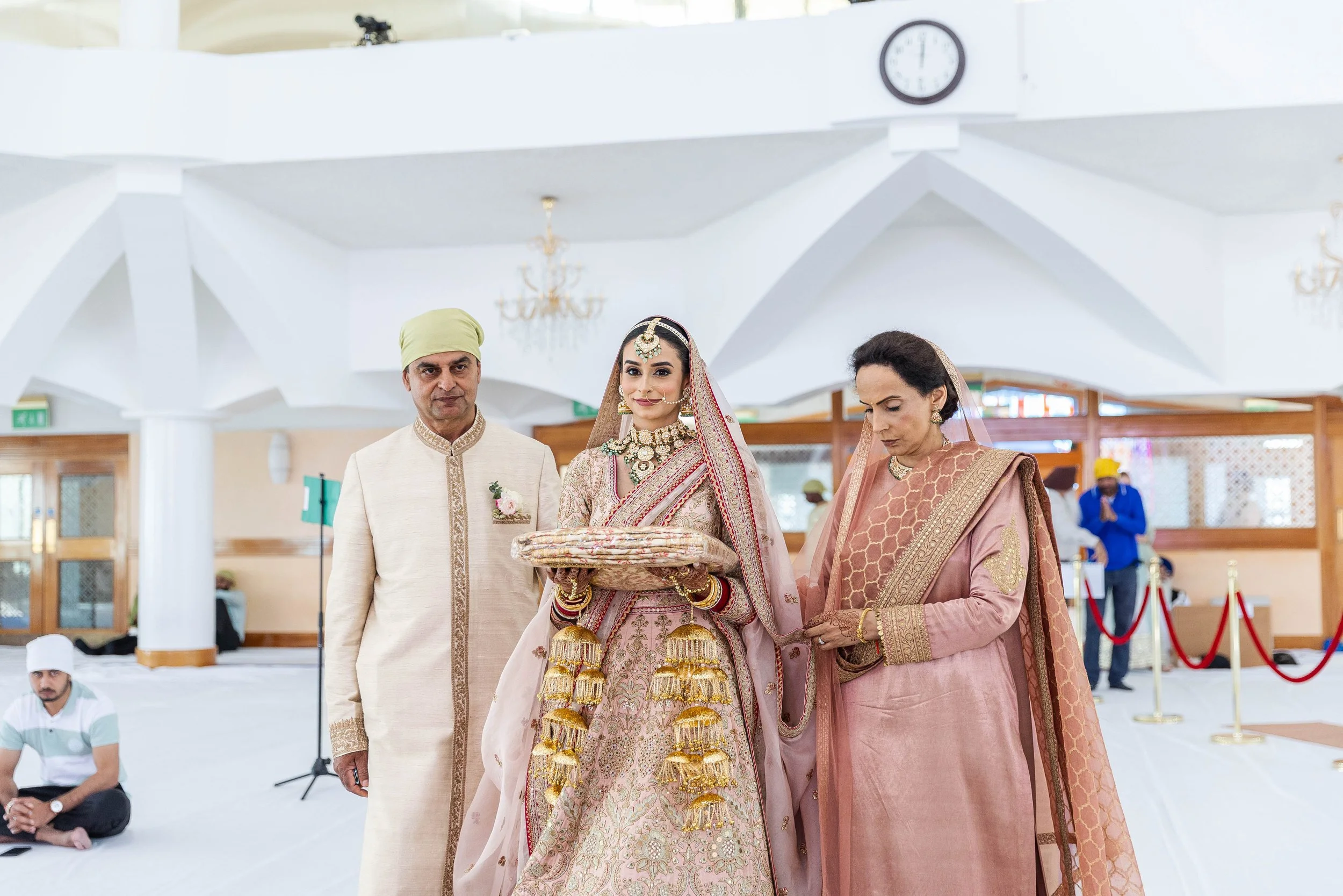 Indian bride holding a tray during a wedding ceremony, with two women and a man standing beside her, inside a decorated hall.