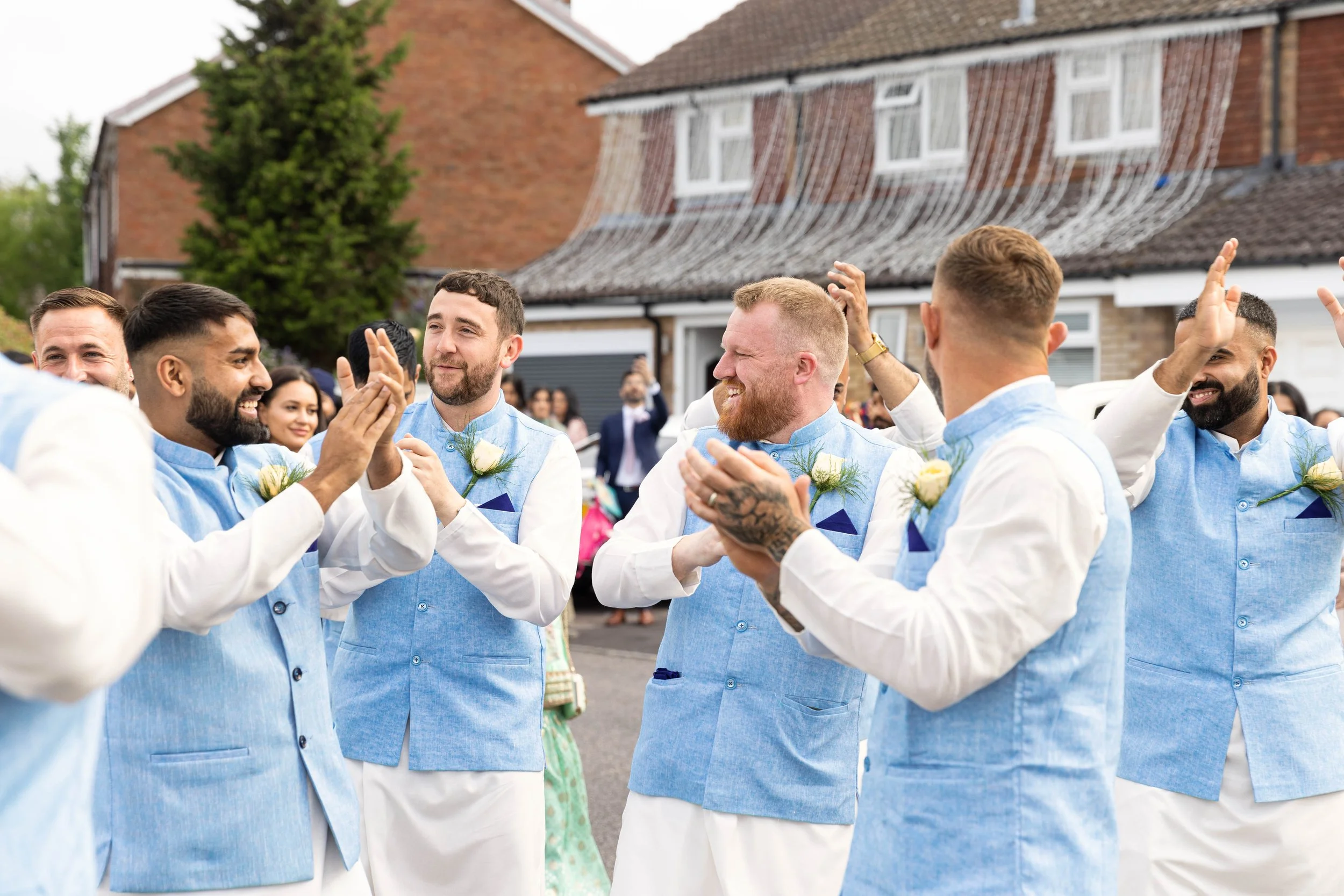 Group of men in matching blue and white vests celebrating outdoors at a wedding reception.