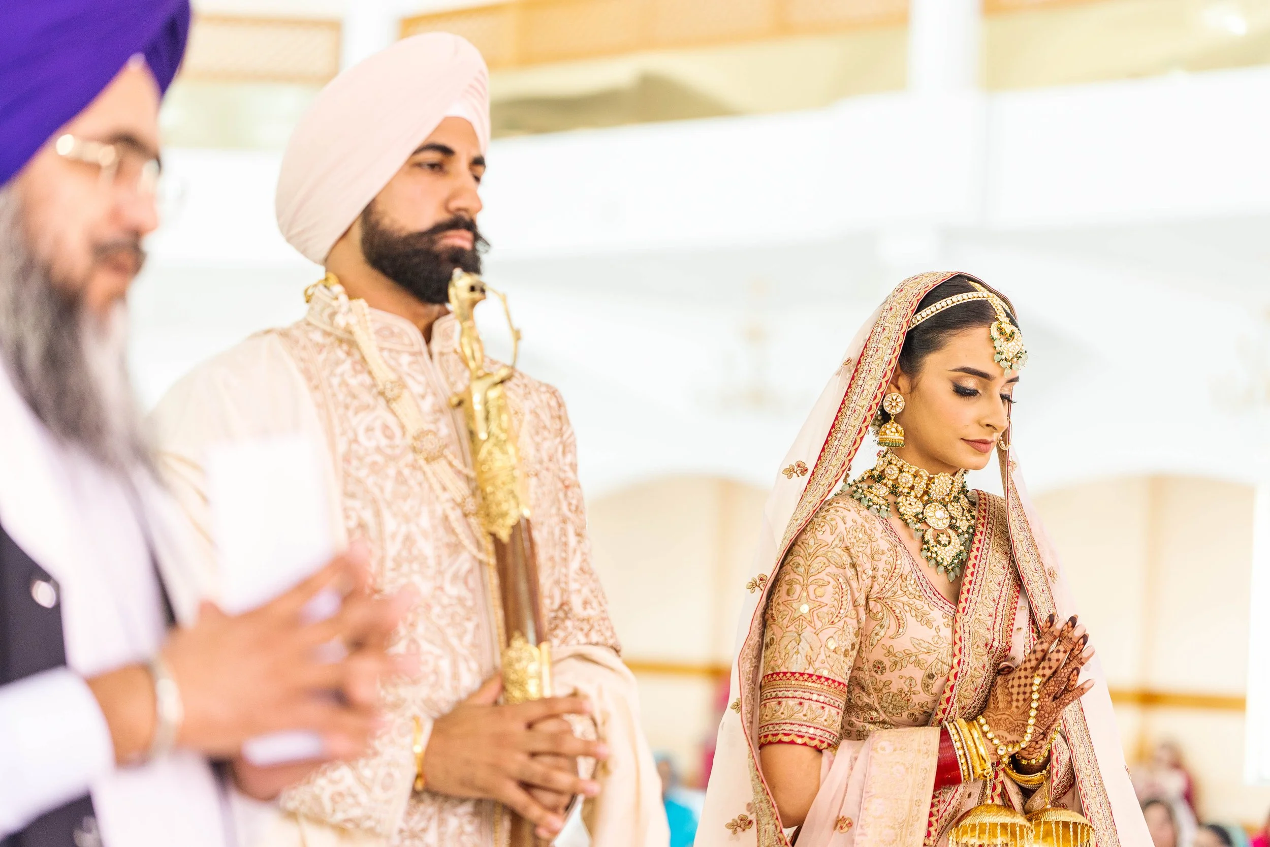 Indian wedding ceremony with a bride and groom, dressed in traditional attire, praying with hands folded, attended by elder family members.