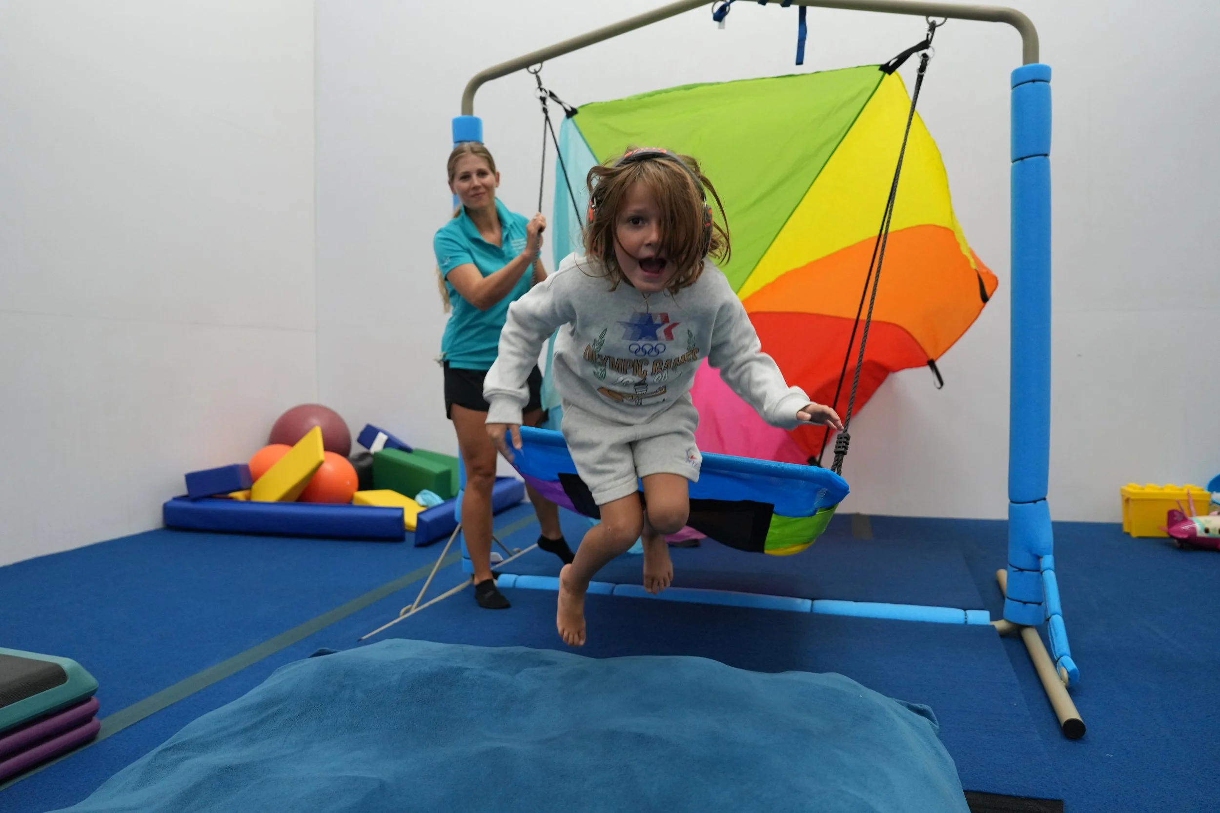 Child using suspended sensory equipment during occupational therapy to address regulation, coordination, and motor planning.