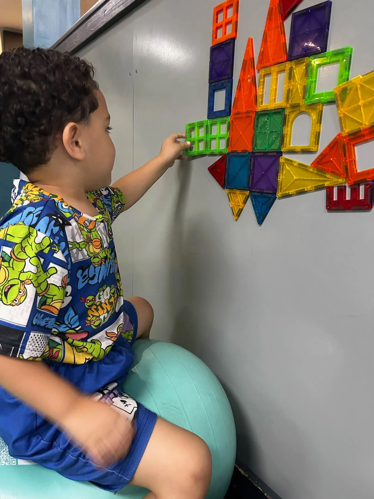 Child building with magnetic tiles on a vertical surface during an occupational therapy visual-motor activity.