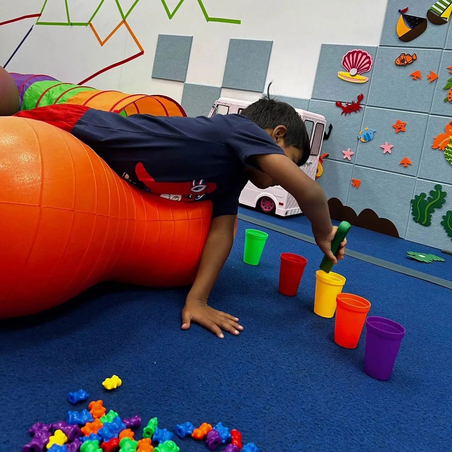 Child weight-bearing over a therapy ball while reaching and sorting small objects during pediatric occupational therapy at Apollo Beach Therapy Center.