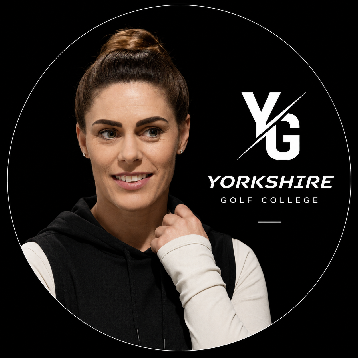 A young woman with brown hair in a high bun wearing a black and white hoodie, smiling in front of a black background with the Yorkshire Golf Academy logo.