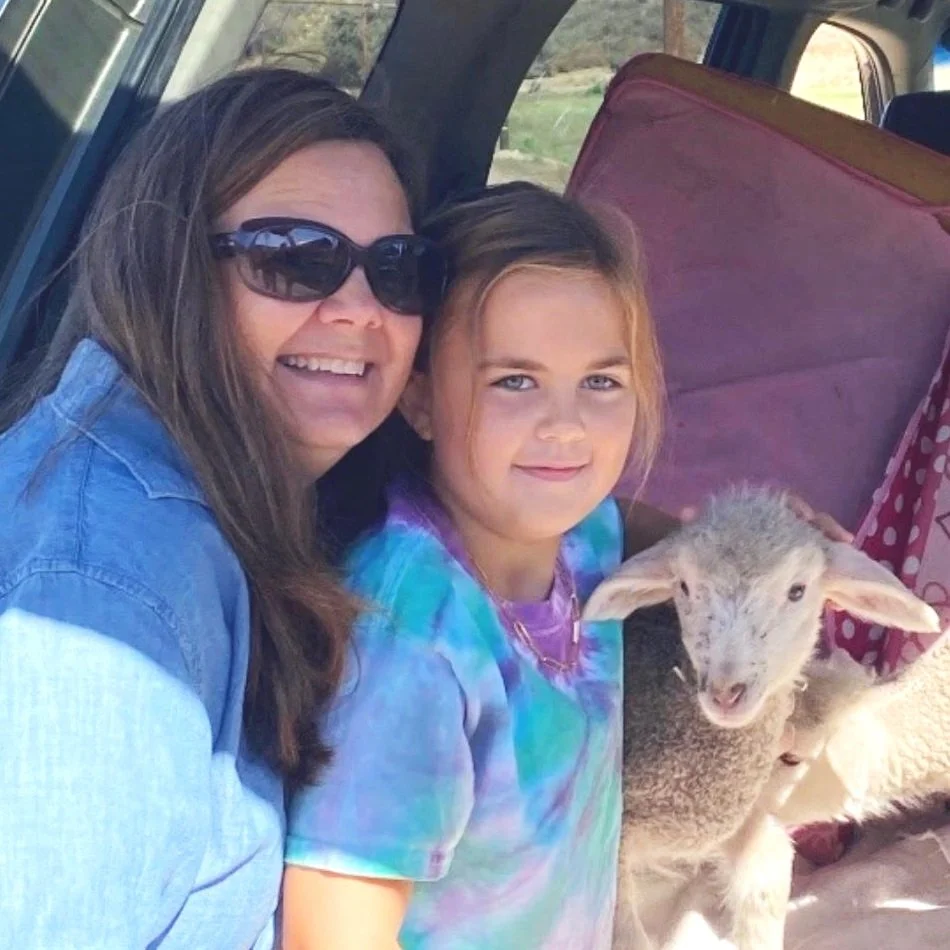 Woman and girl smiling while holding a lamb inside a vehicle.