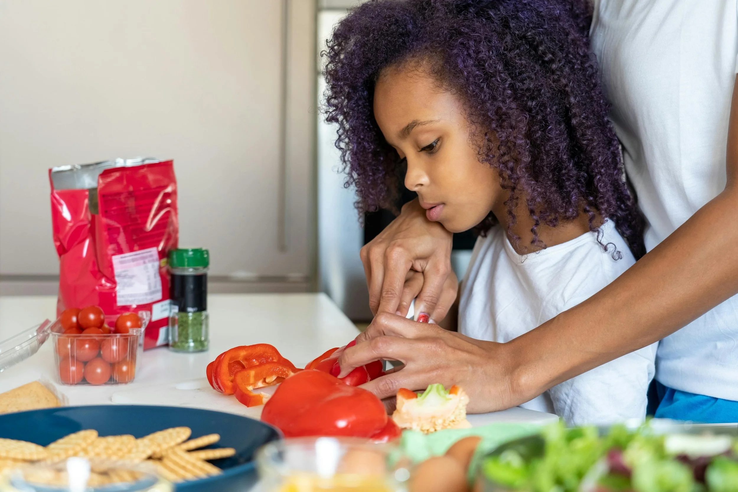A young girl helping her mom cut vegetables
